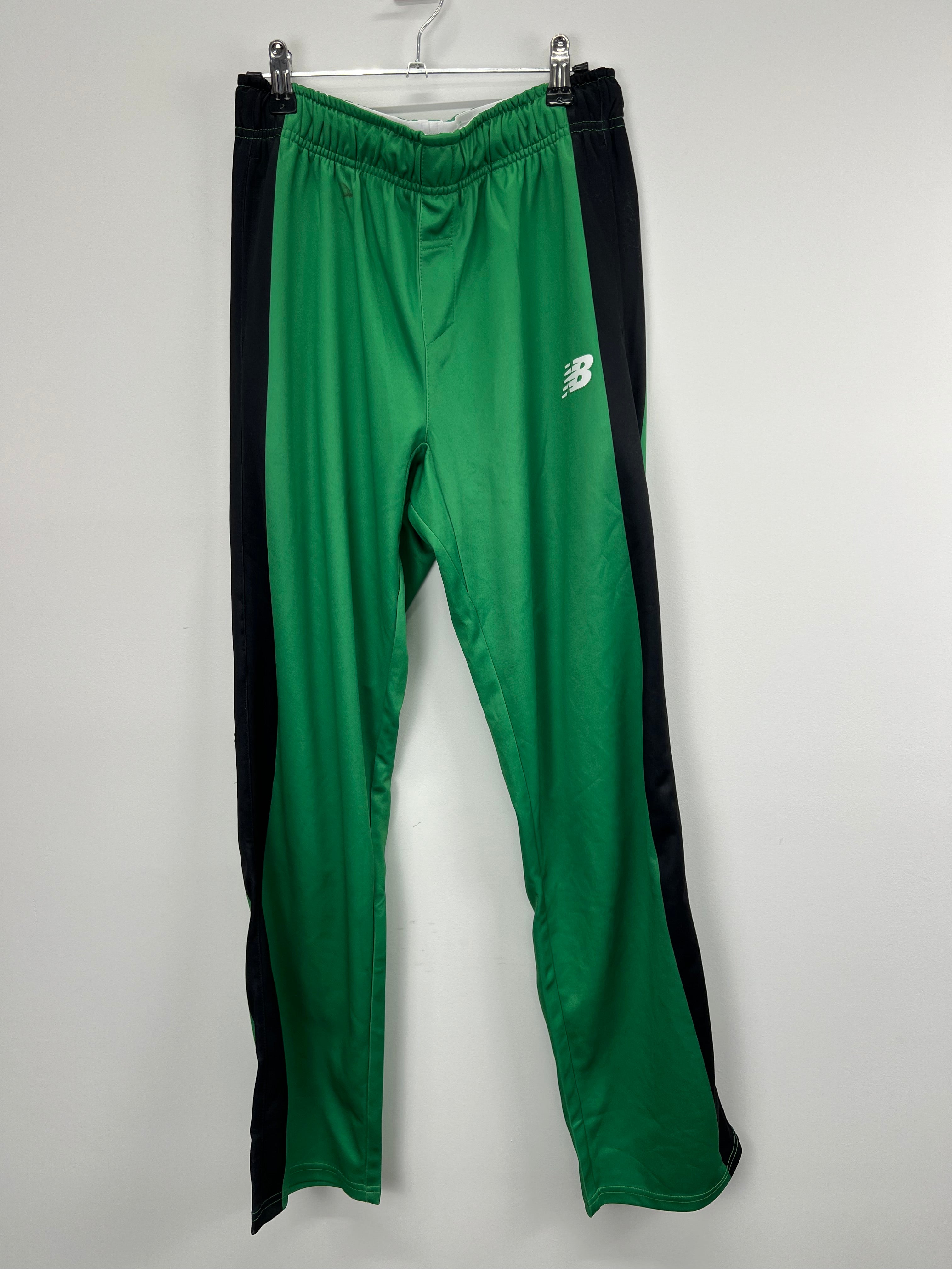 front view of women's green New Balance tracksuit bottoms with black side stripes hanging on clip hanger