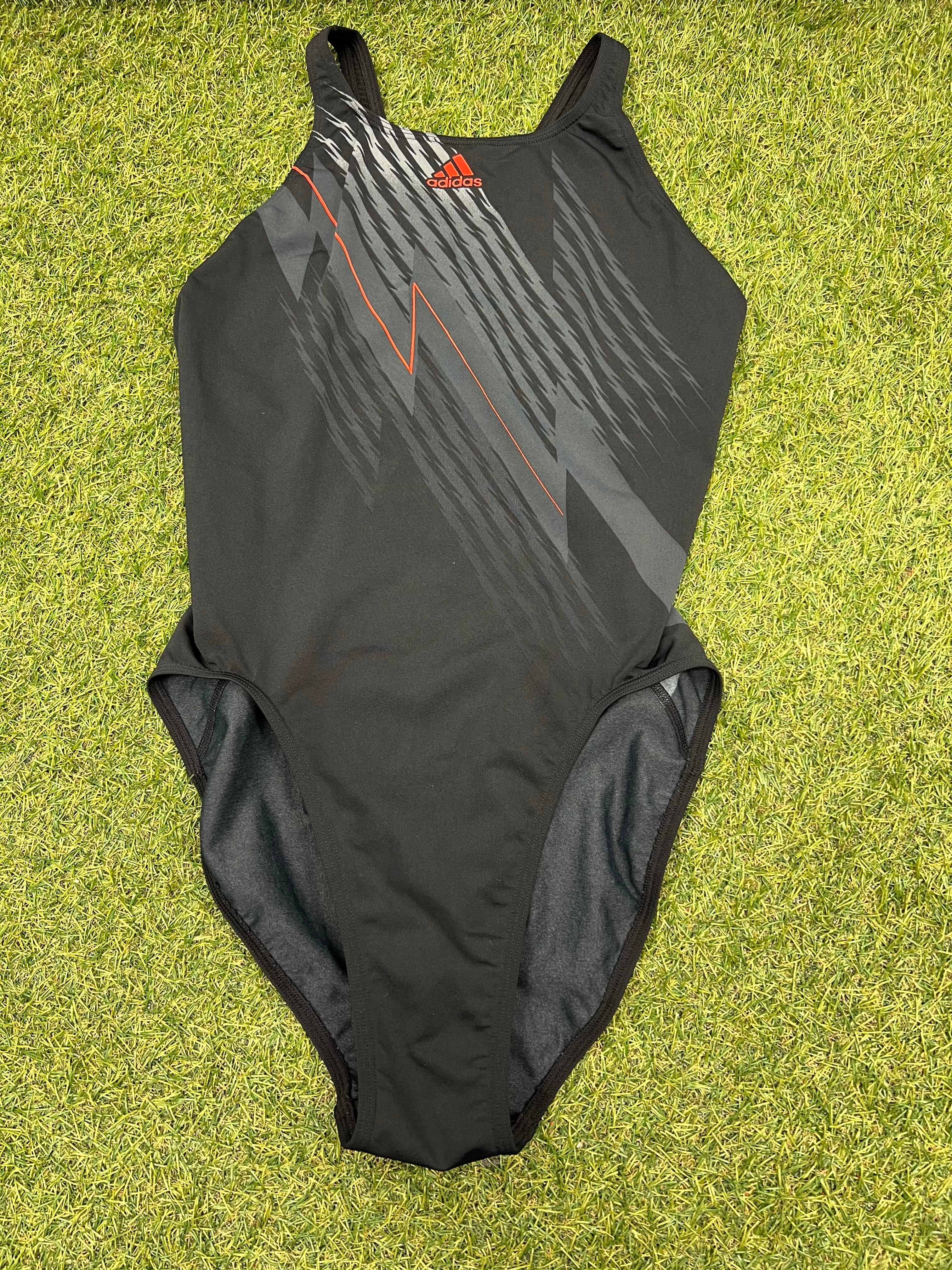 Front view of Adidas Infinitex black swimsuit with grey and orange graphic design on green grass