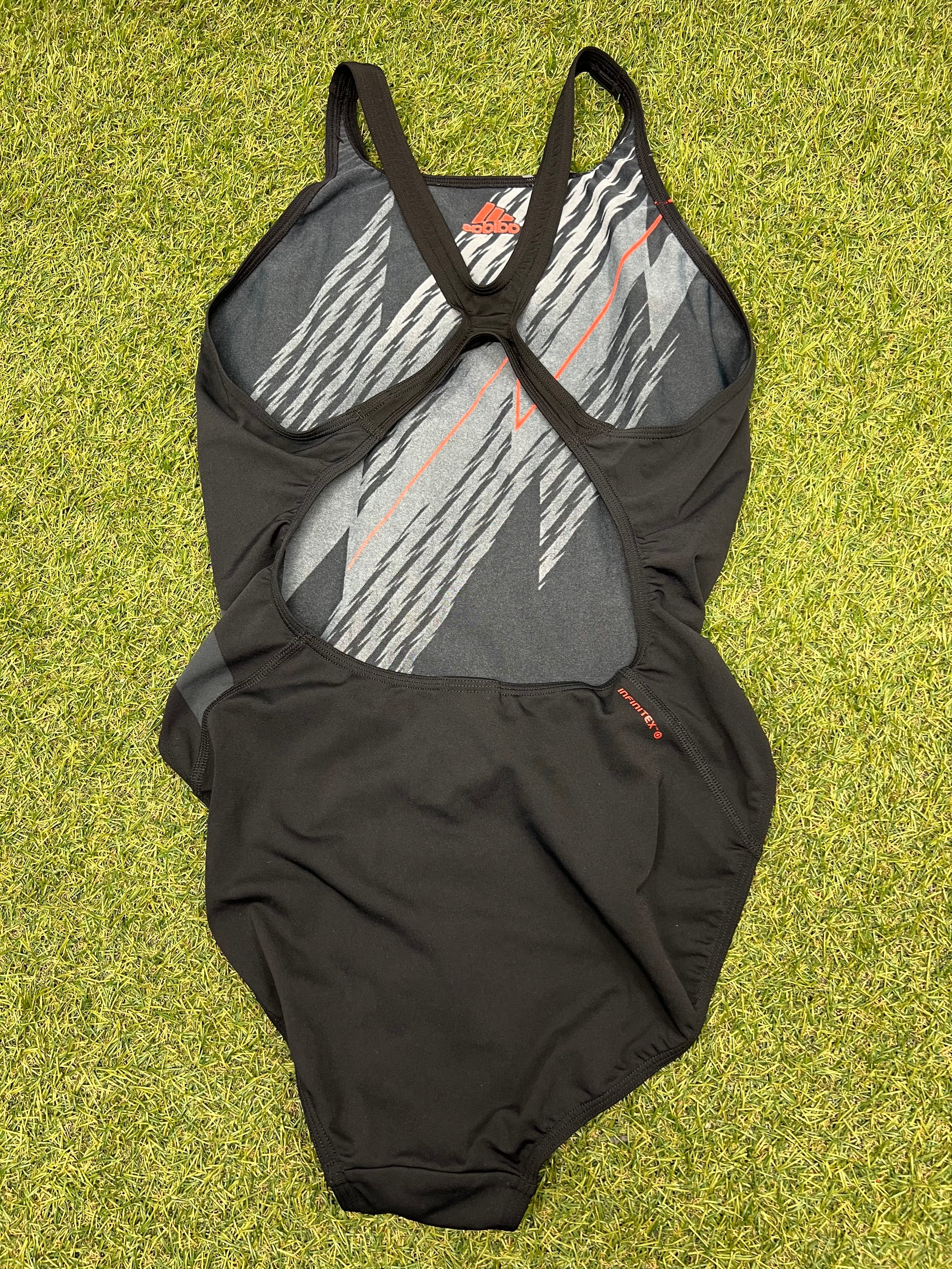 Back view of Adidas Infinitex black swimsuit showing cut-out back design with racer straps on green grass