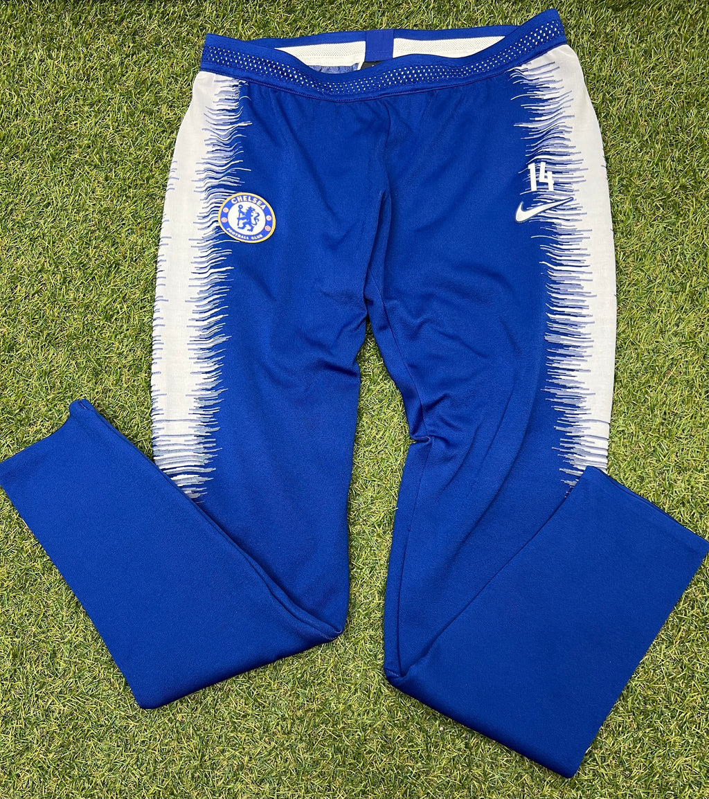 Front view of Chelsea FC royal blue training joggers with white brushstroke side panels on grass