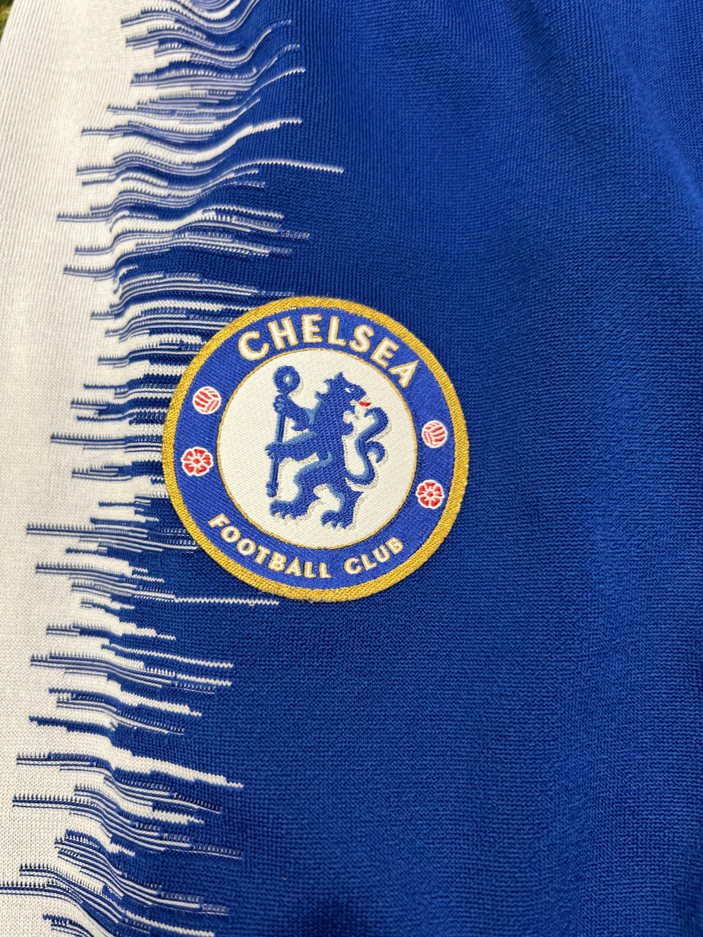 Close-up of embroidered Chelsea FC badge on left hip of blue training joggers