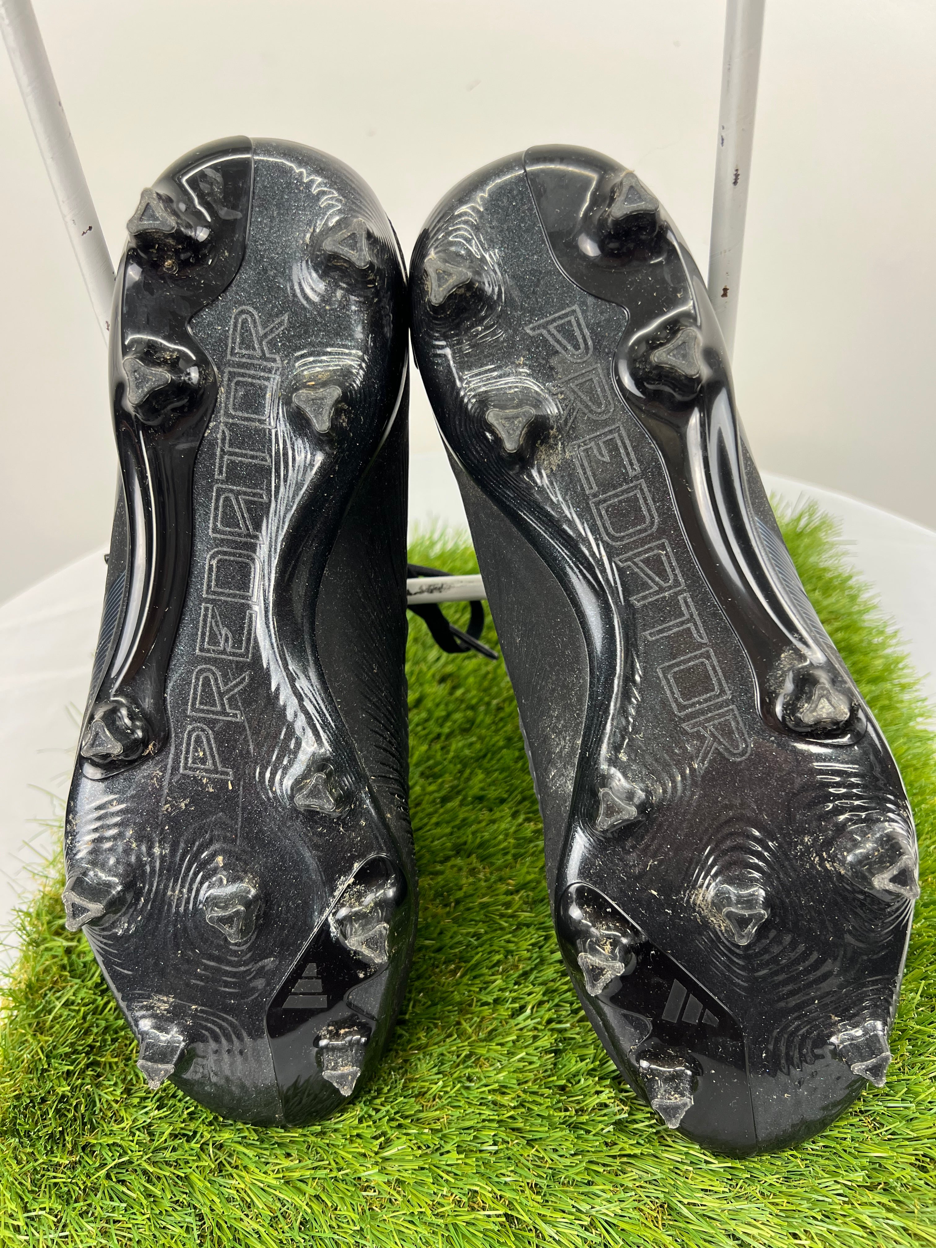 Sole view of Adidas Predator boots showing triangular firm ground studs and branding on artificial grass
