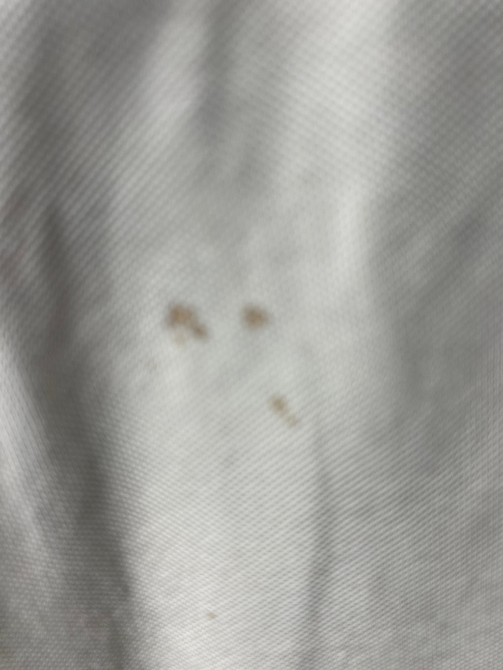Close-up detail of light marks and stains on front of white sleeveless jumper