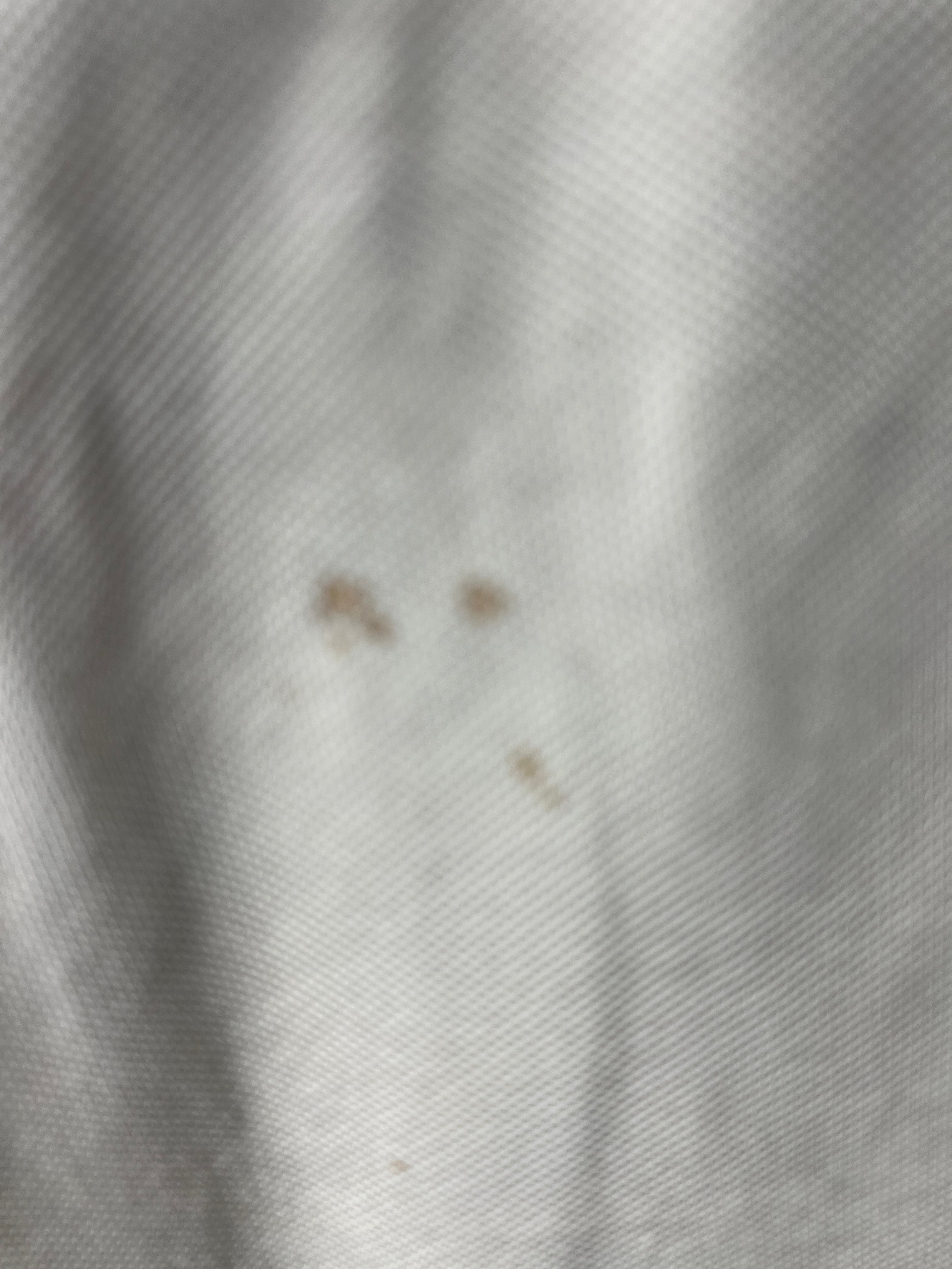 Close-up detail of light marks and stains on front of white sleeveless jumper
