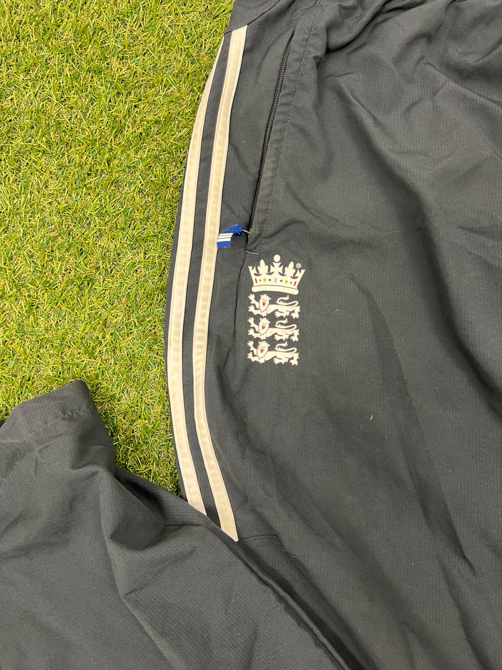 Close-up of left front pocket with England cricket logo and zipper detail on black trousers