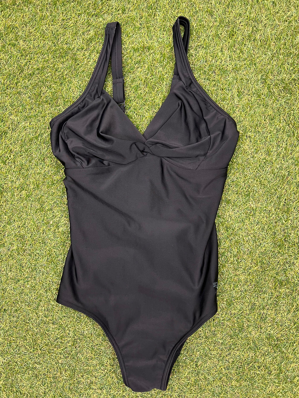 Front view of black Speedo one-piece swimsuit with twisted front detail on grass