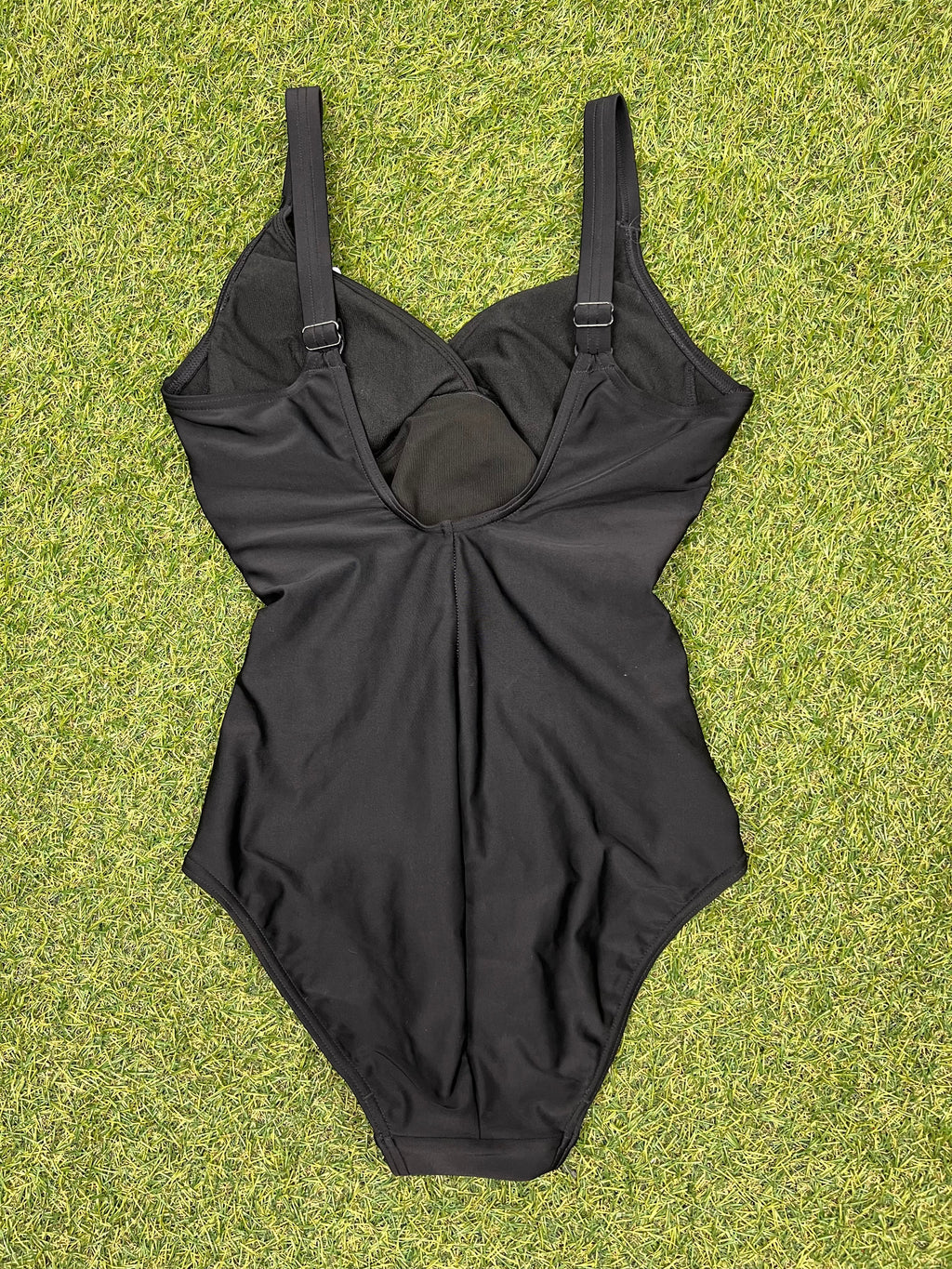 Back view of Speedo black one-piece swimsuit showing adjustable straps on grass