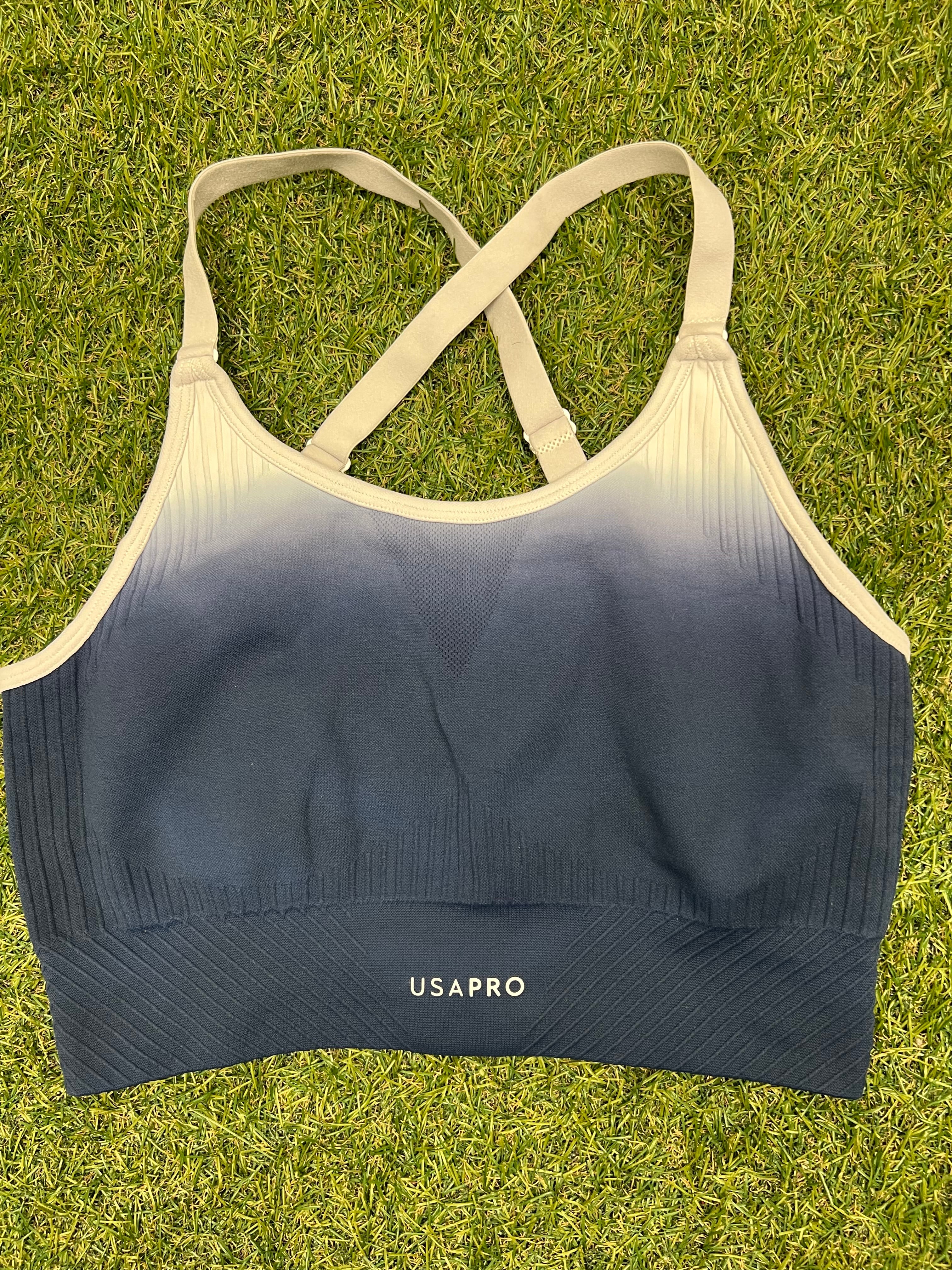 Front view of USA Pro sports bra top in blue gradient with white straps on grass