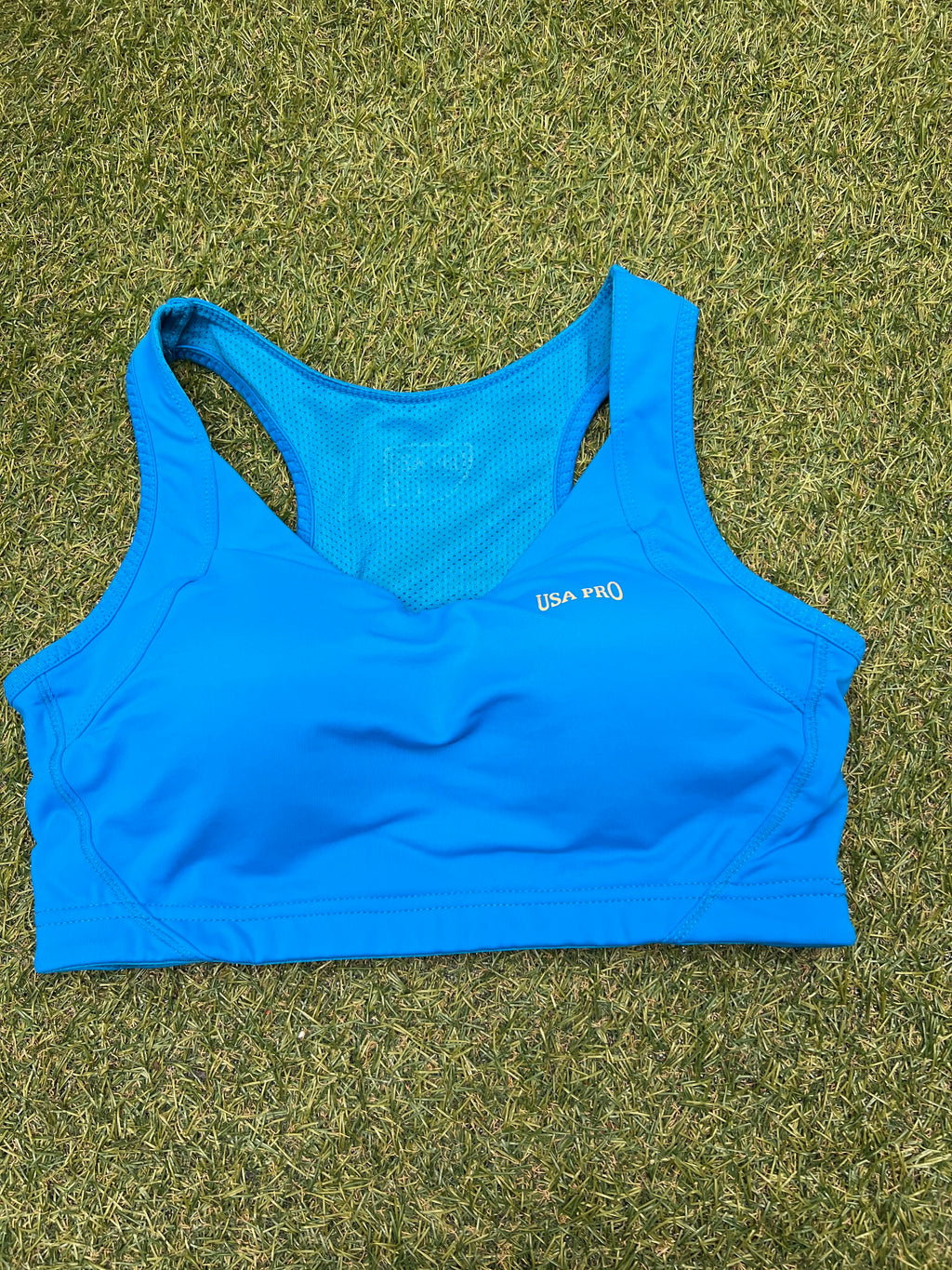 Front view of USA Pro turquoise sports bra laid flat on grass