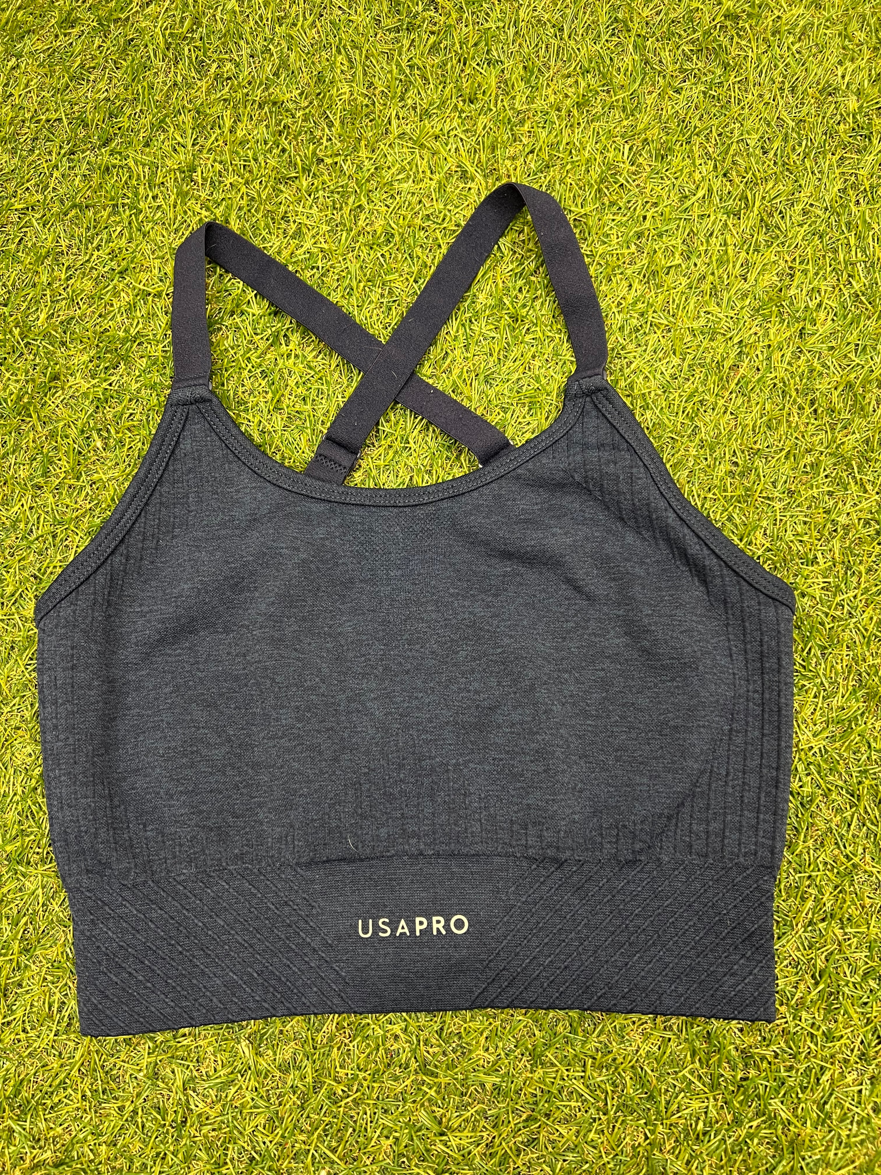 Front view of USA Pro navy marl sports bra top with ribbed hem on grass background