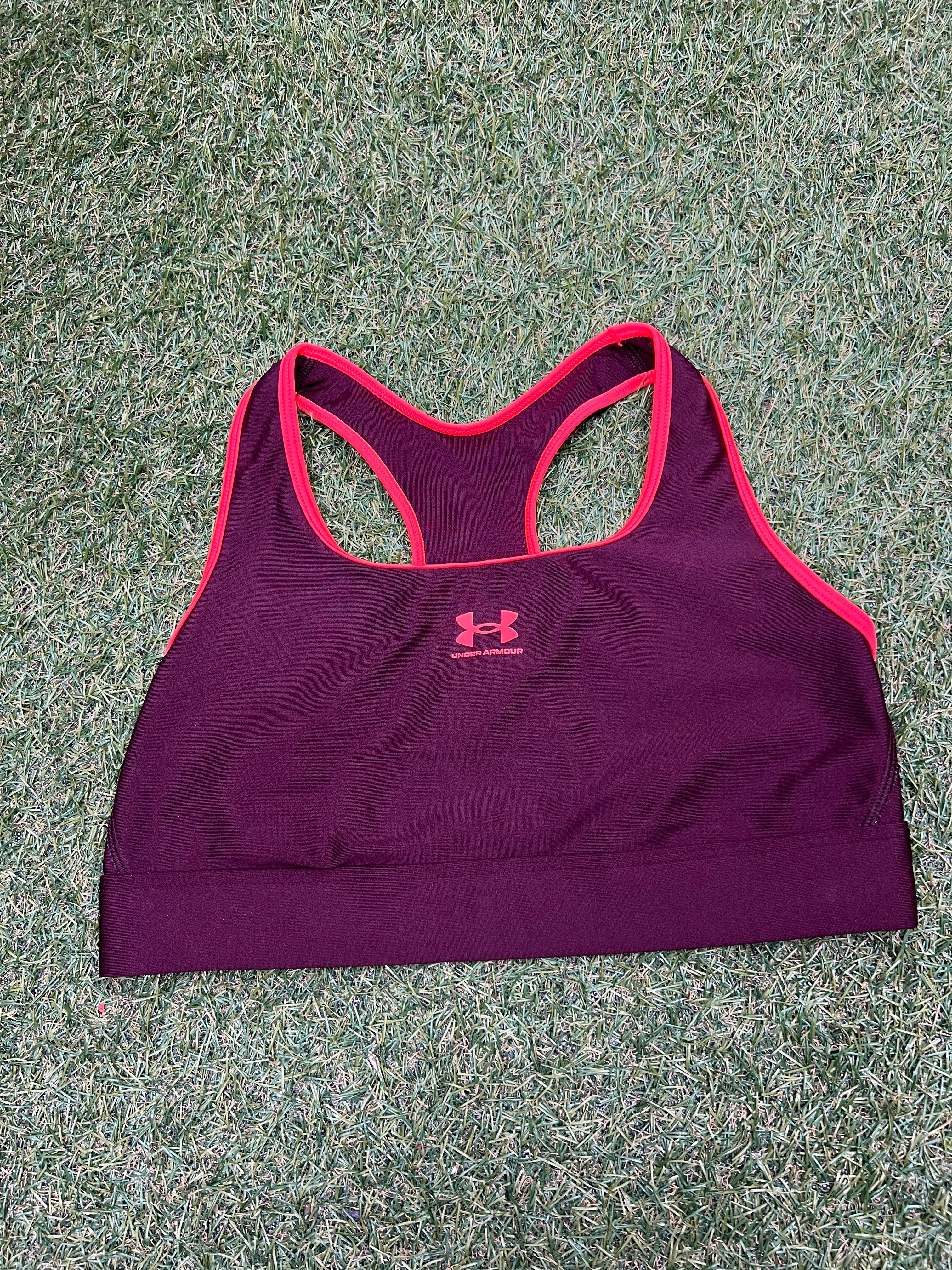 Front view of Under Armour sports bra in burgundy with pink trim laid flat on grass
