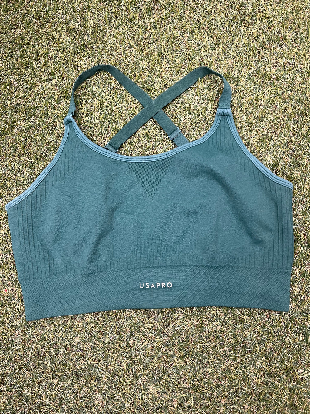 Front view of USA Pro green seamless sports bra top laid on grass