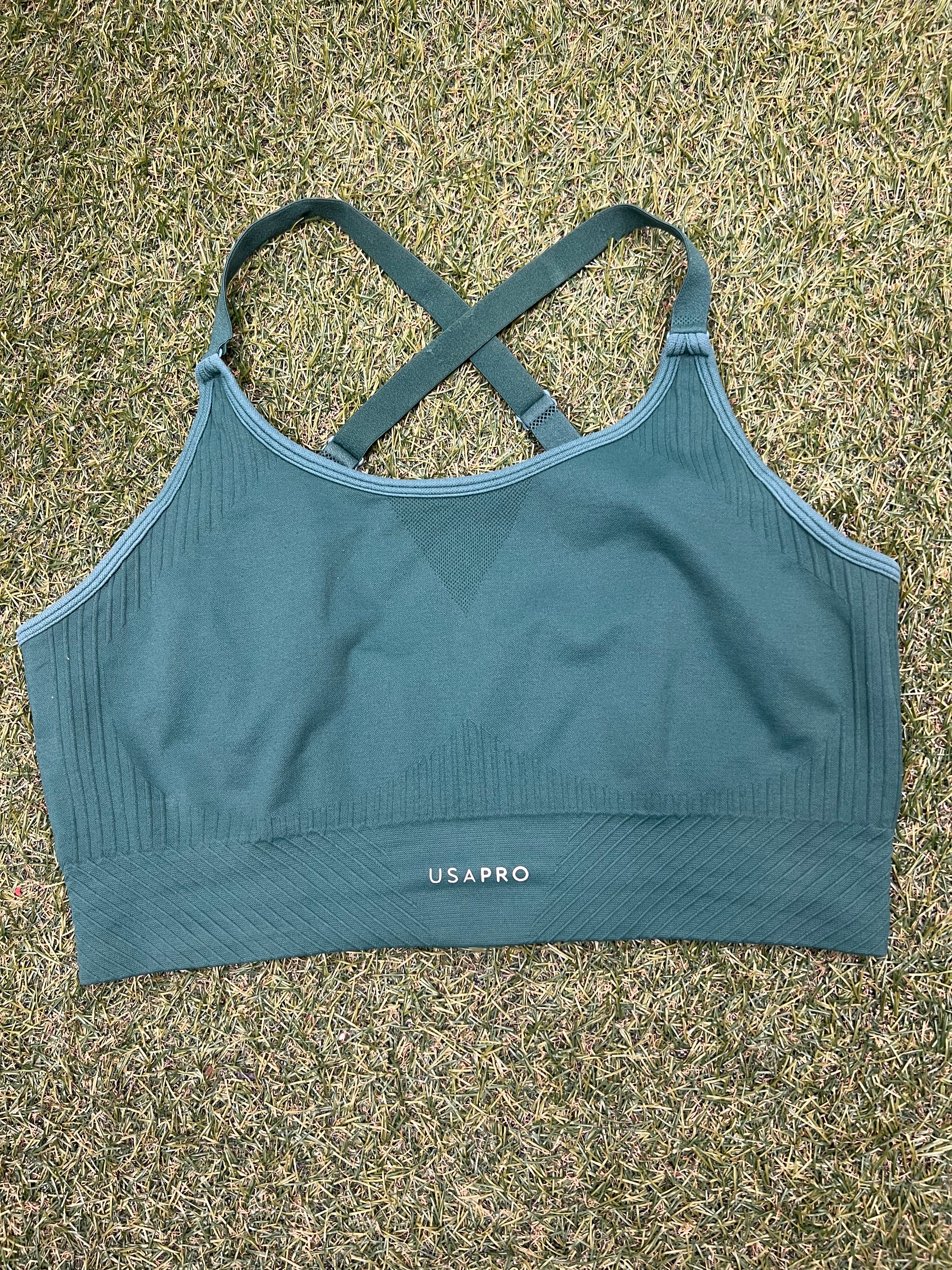 Front view of USA Pro green seamless sports bra top laid on grass