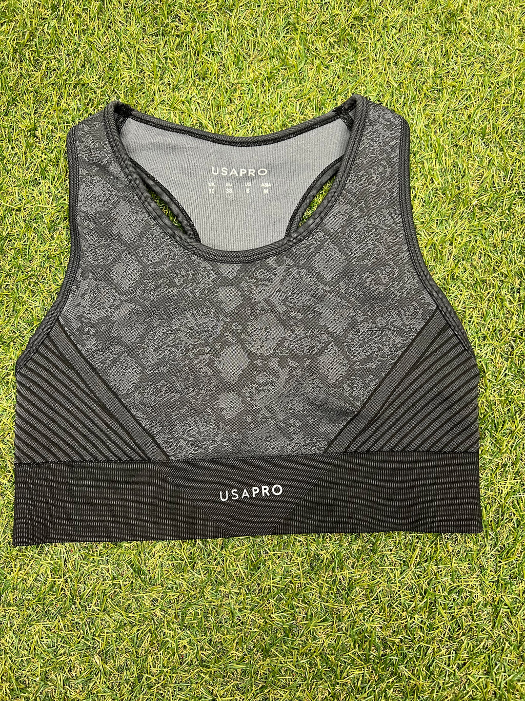 Front view of grey and black USA Pro sports bra with snakeskin pattern on grass background