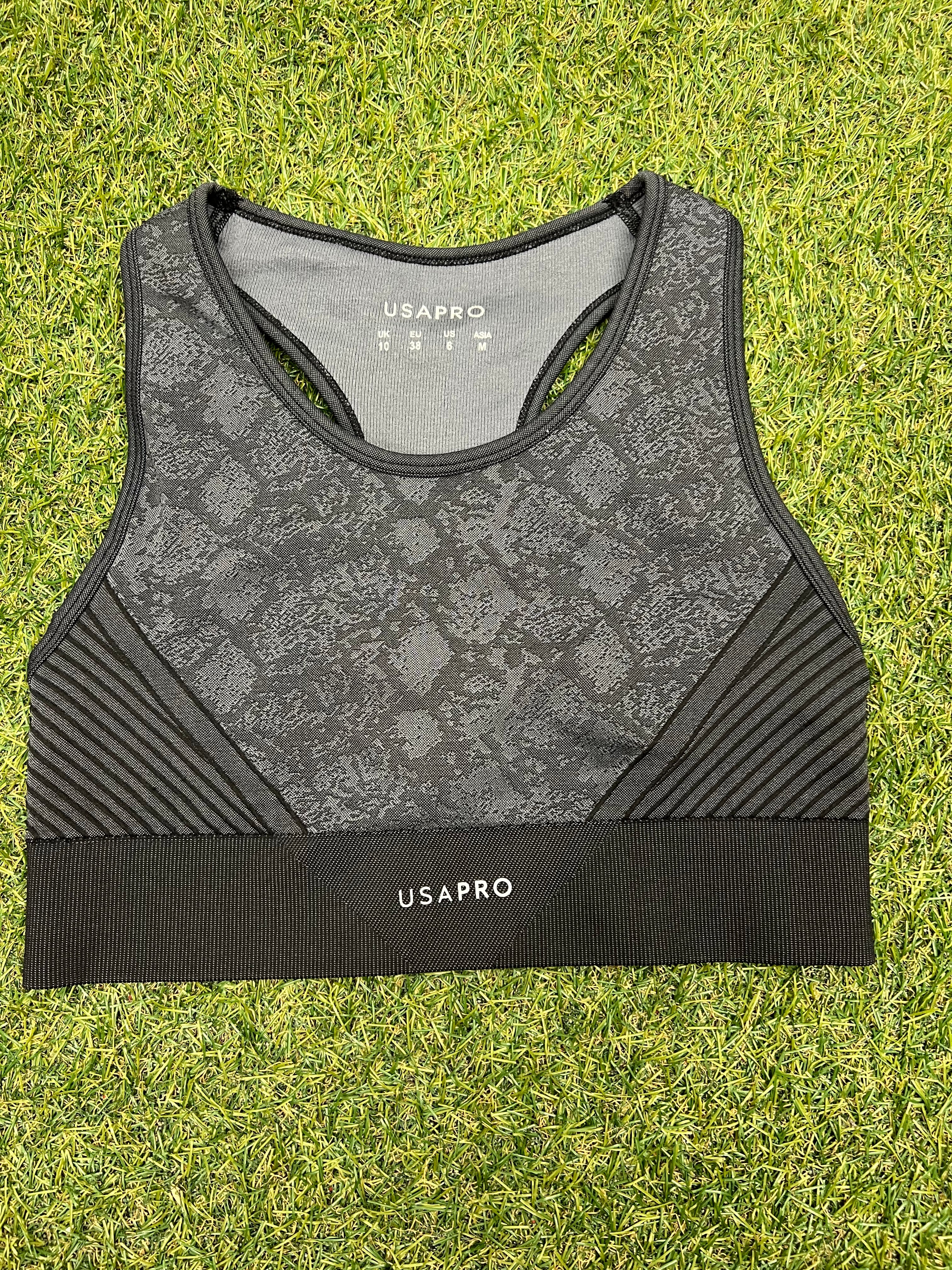 Front view of grey and black USA Pro sports bra with snakeskin pattern on grass background