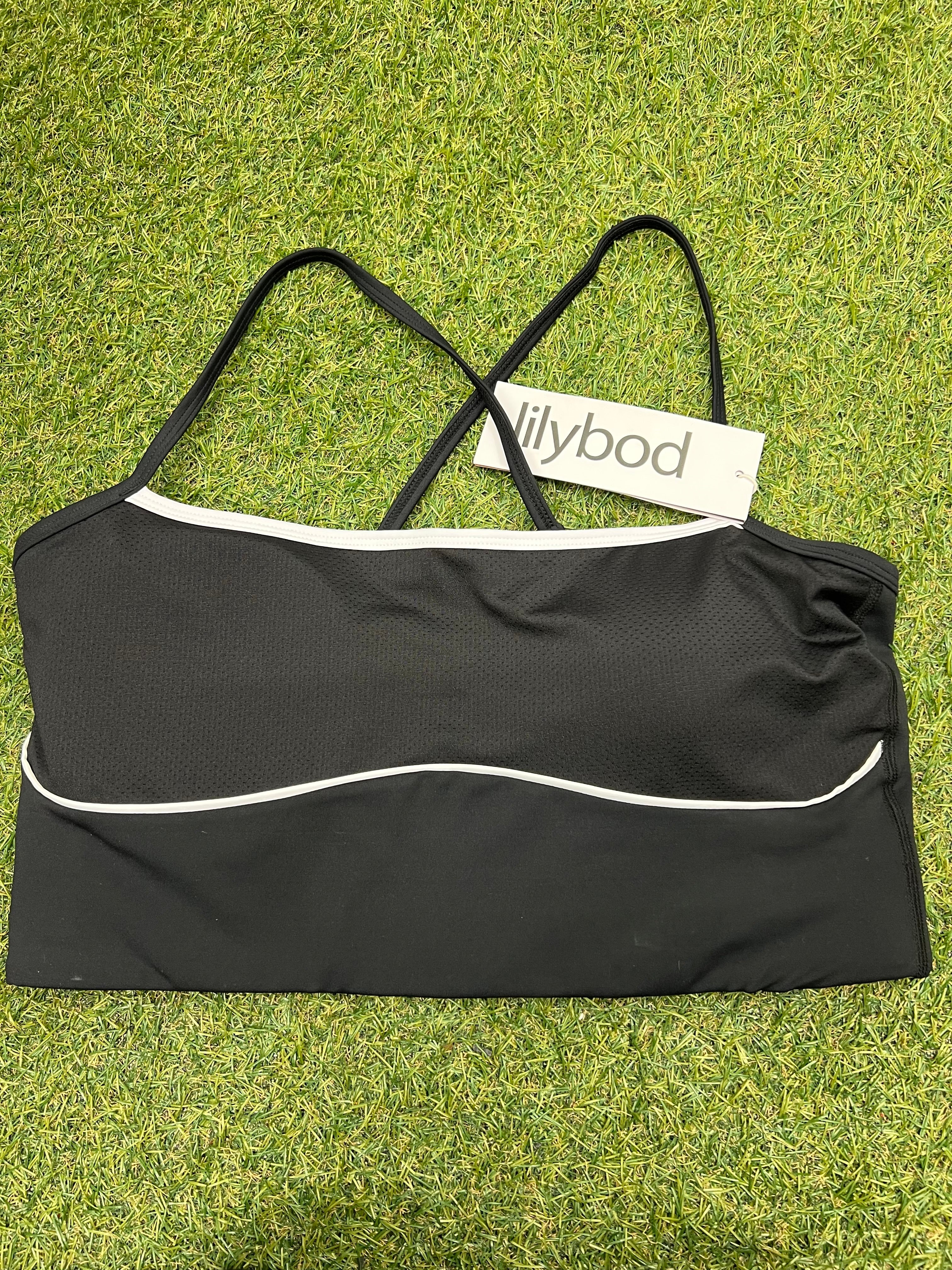 Lilybod black sports bra top front view with white piping and thin straps on grass background