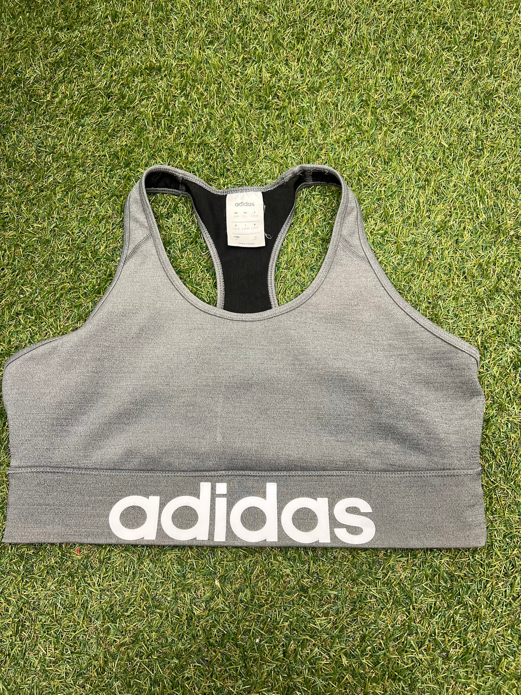 Front view of grey Adidas sports bra top with white logo on grass