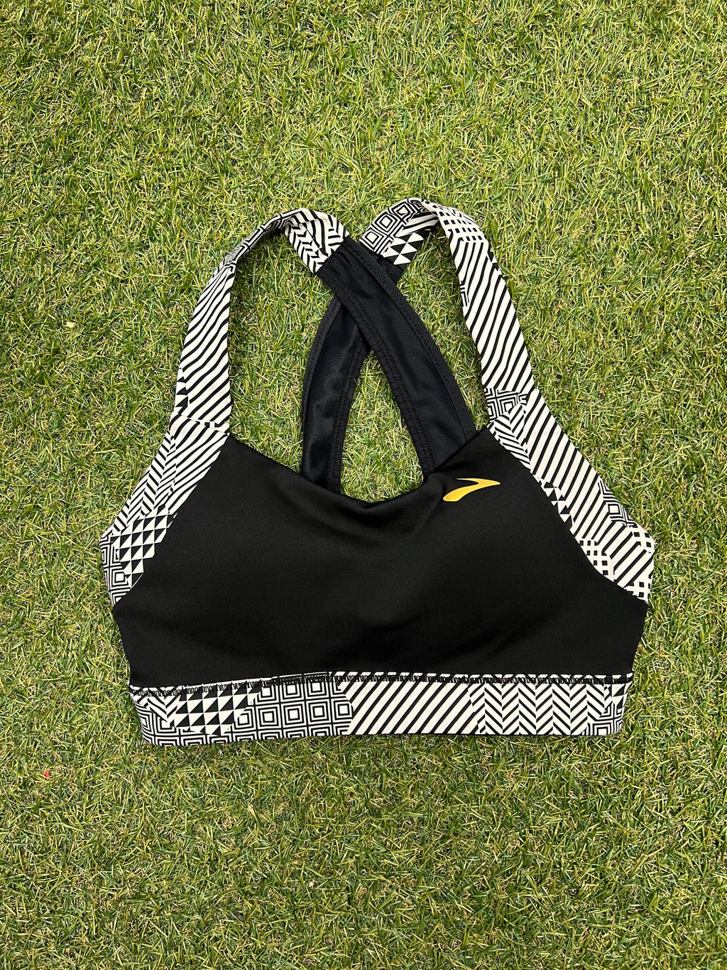 Brooks black sports bra laid flat on grass showing front with black and white geometric strap detail