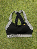 Brooks black sports bra laid flat on grass showing front with black and white geometric strap detail