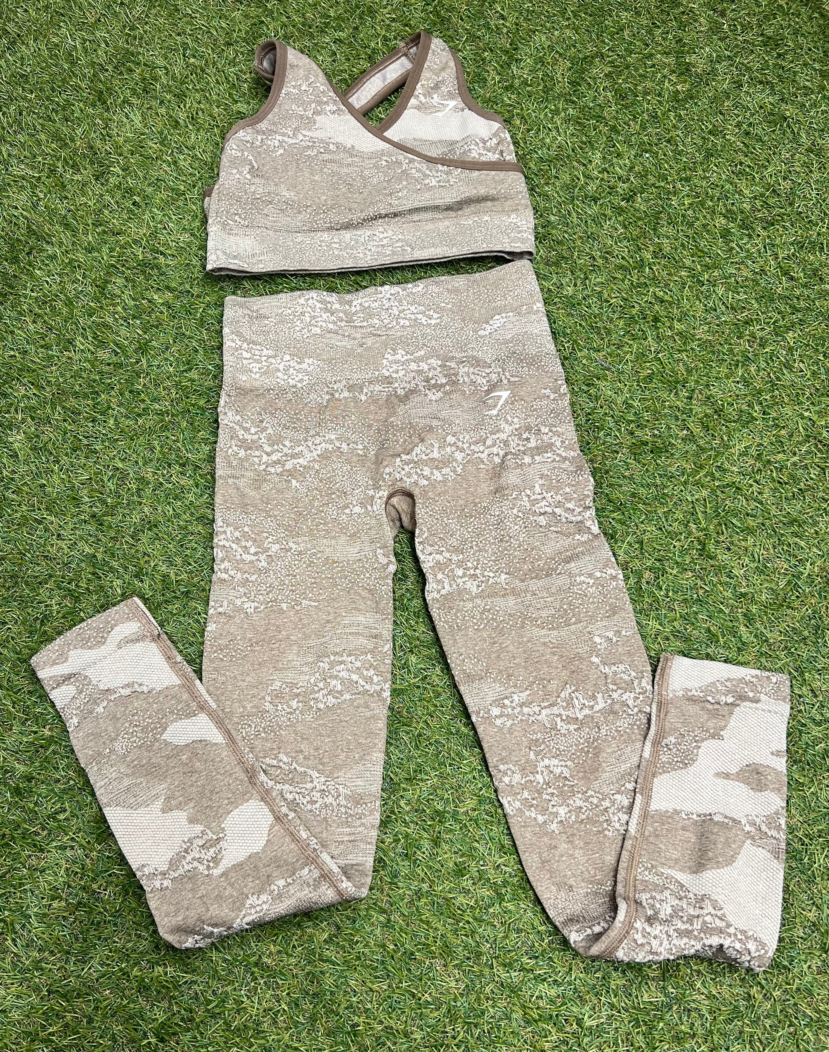 Front view of Gymshark seamless sports bra and leggings set in beige camouflage pattern on grass