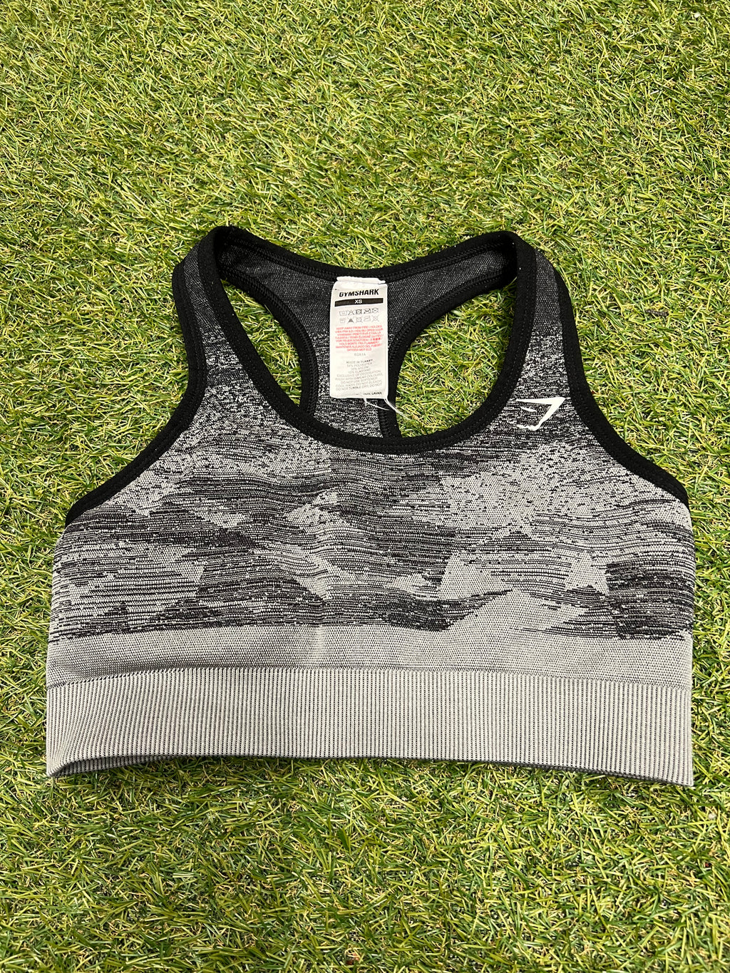 Front view of Gymshark seamless sports bra top in black and grey laid flat on grass