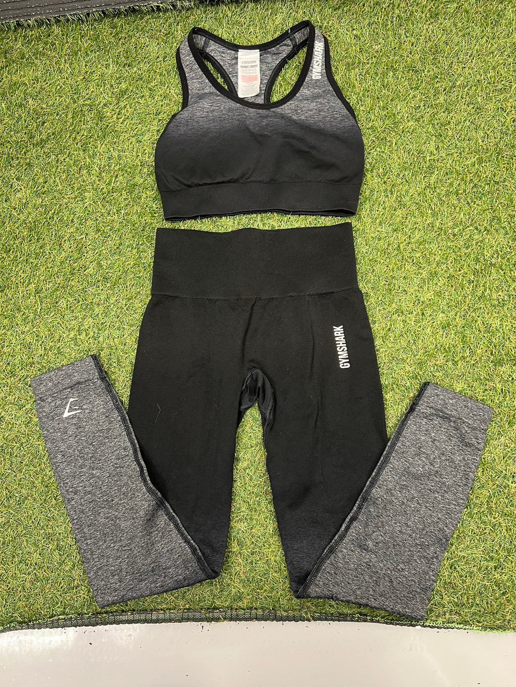 Gymshark black and grey sports bra and leggings laid flat on grass, front view