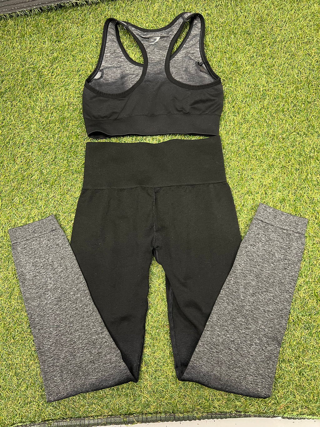 Gymshark black and grey sports bra and leggings laid flat on grass, back view