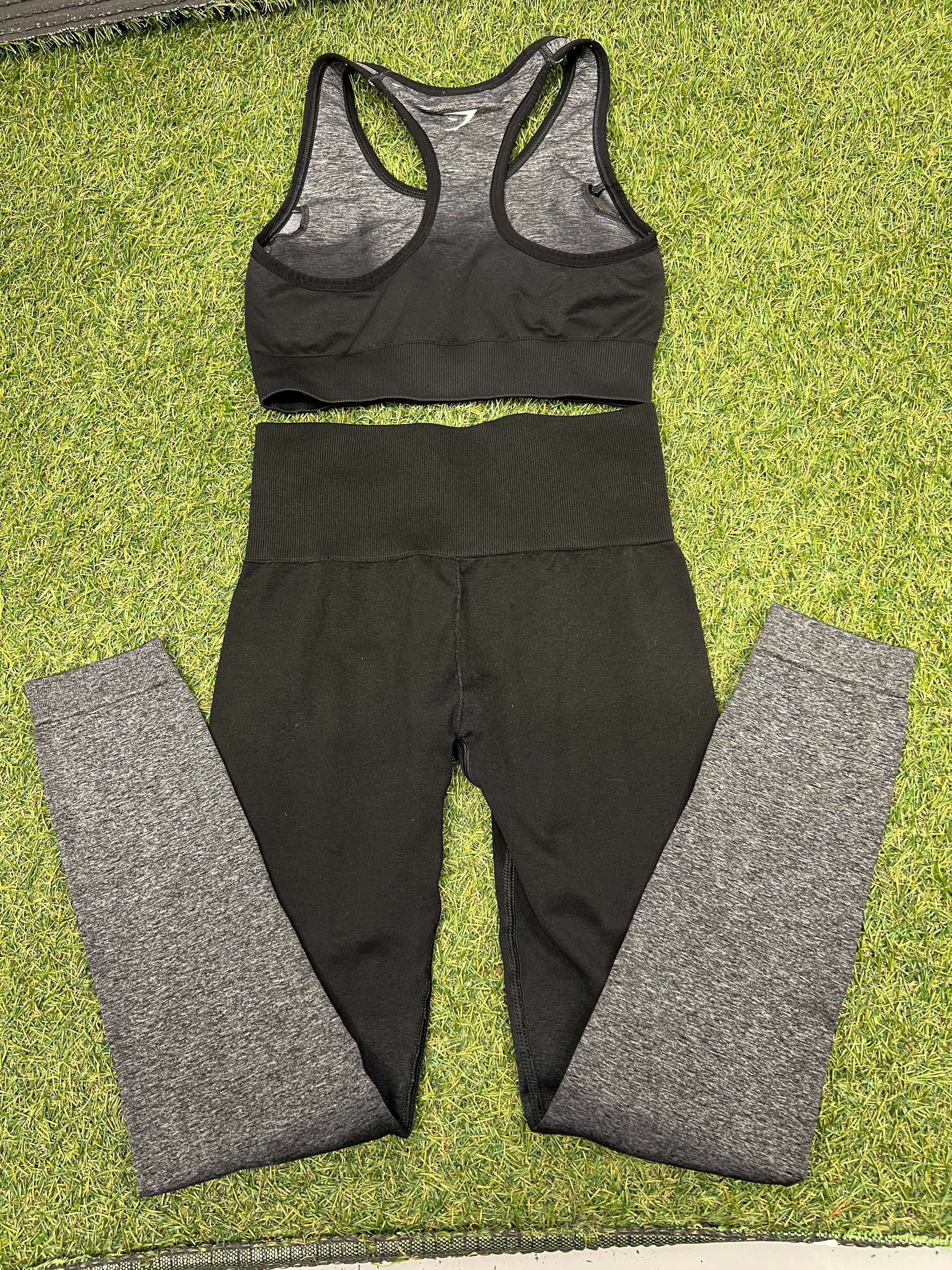 Gymshark black and grey sports bra and leggings laid flat on grass, back view