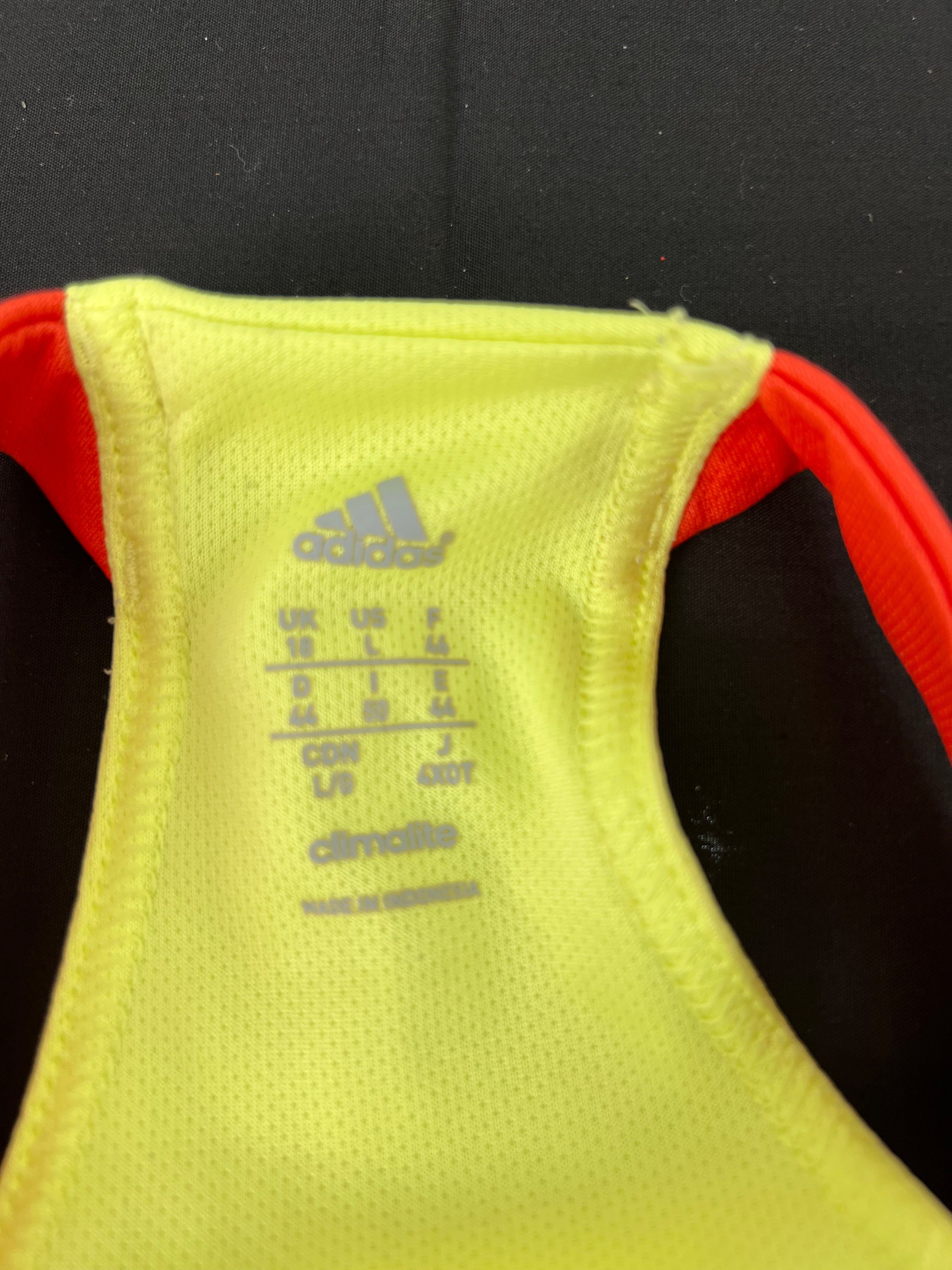 Close-up of Adidas logo and size label inside yellow Climalite sports vest with red straps