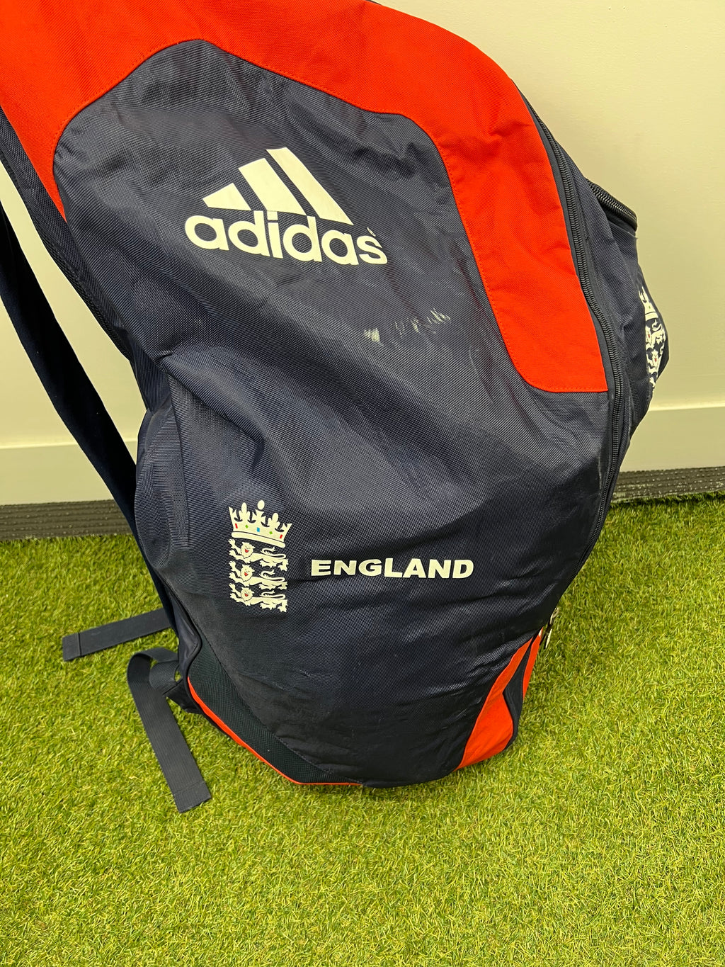 Side angle of cricket bag highlighting red and navy colour blocking and zip compartments
