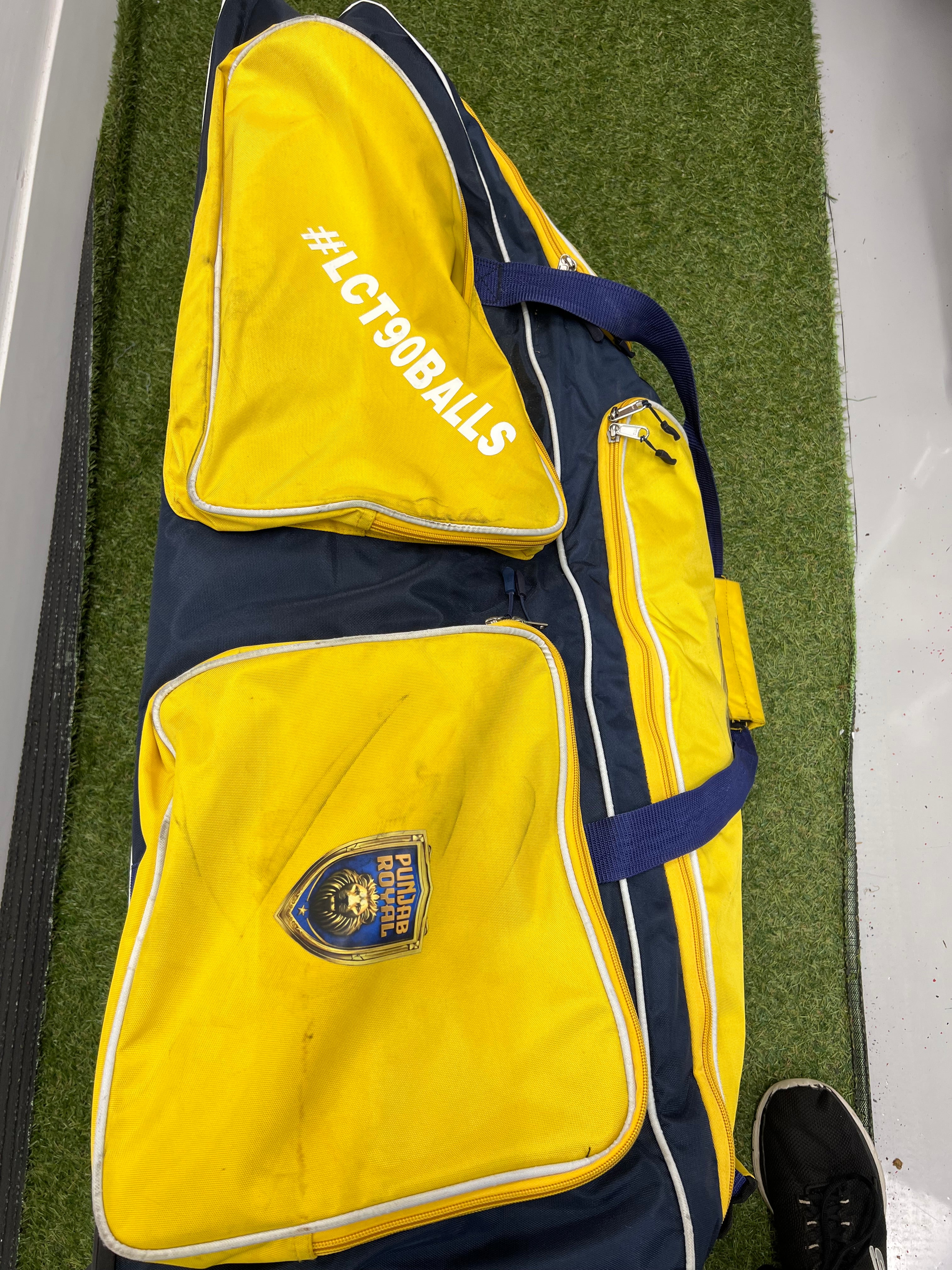 Side view of Punjab Royal cricket bag with #LCT90BALLS text on an outer pocket