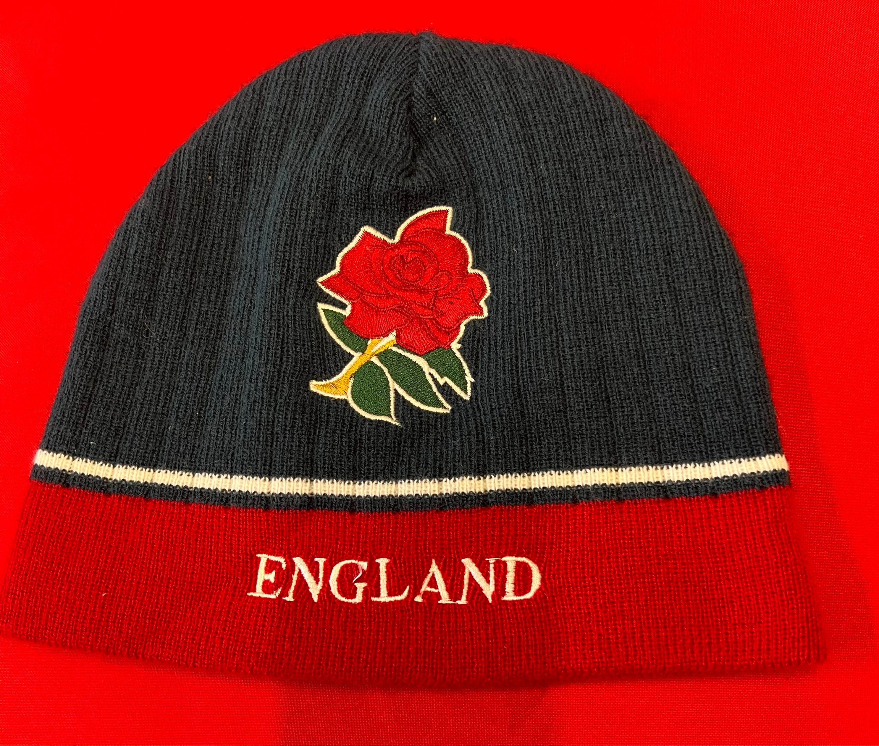 Front view of England Roses rugby beanie hat in navy blue and red with embroidered red rose and England text