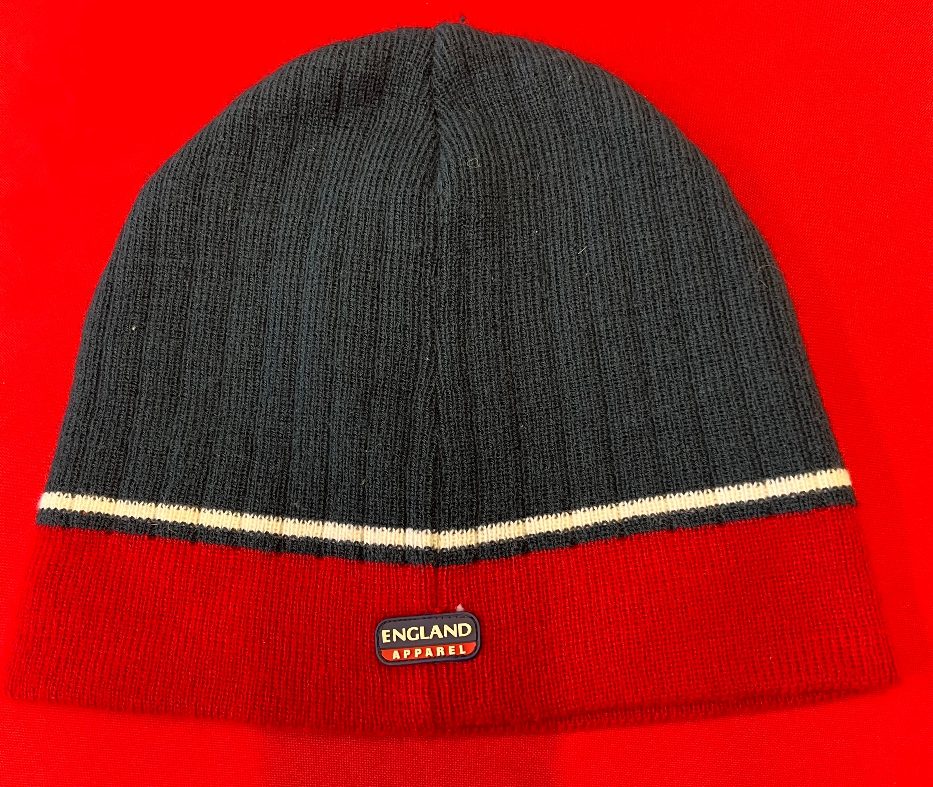 Back view of England Roses rugby beanie hat showing navy blue and red knit design with England Apparel logo tag