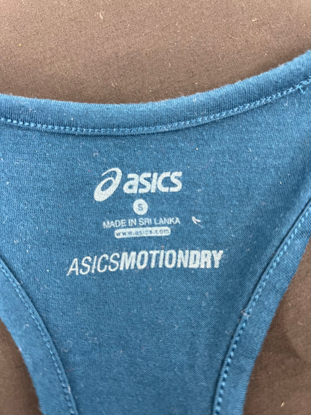Close-up of inner label of Asics blue running vest top indicating size S and MOTIONDRY technology