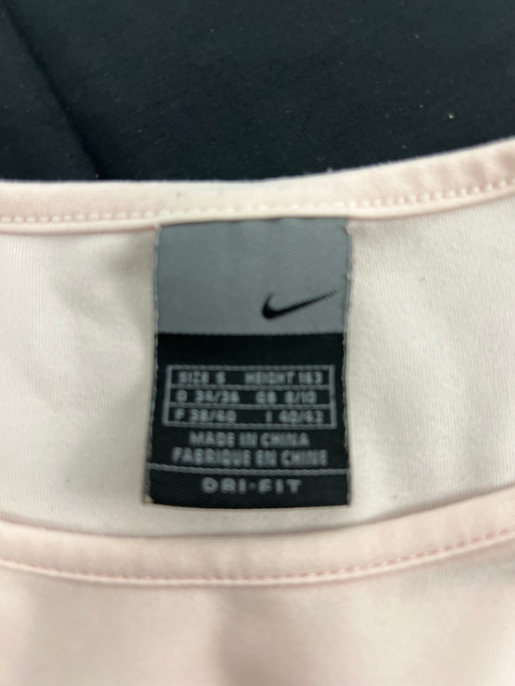Close-up of Nike size and material label inside the light pink t-shirt