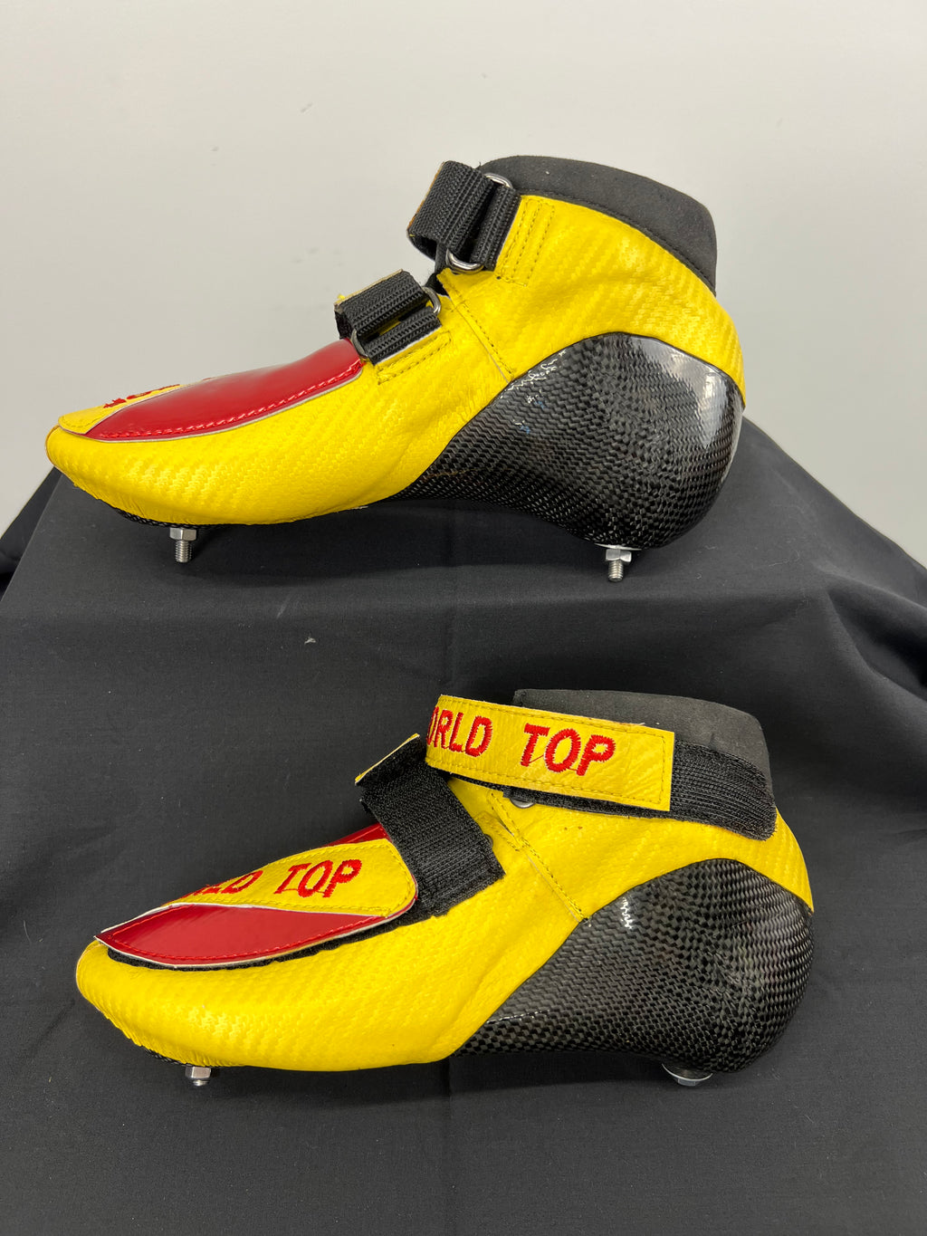 Side view of pair of World Top short track skates in yellow and red with carbon fibre heels and velcro straps