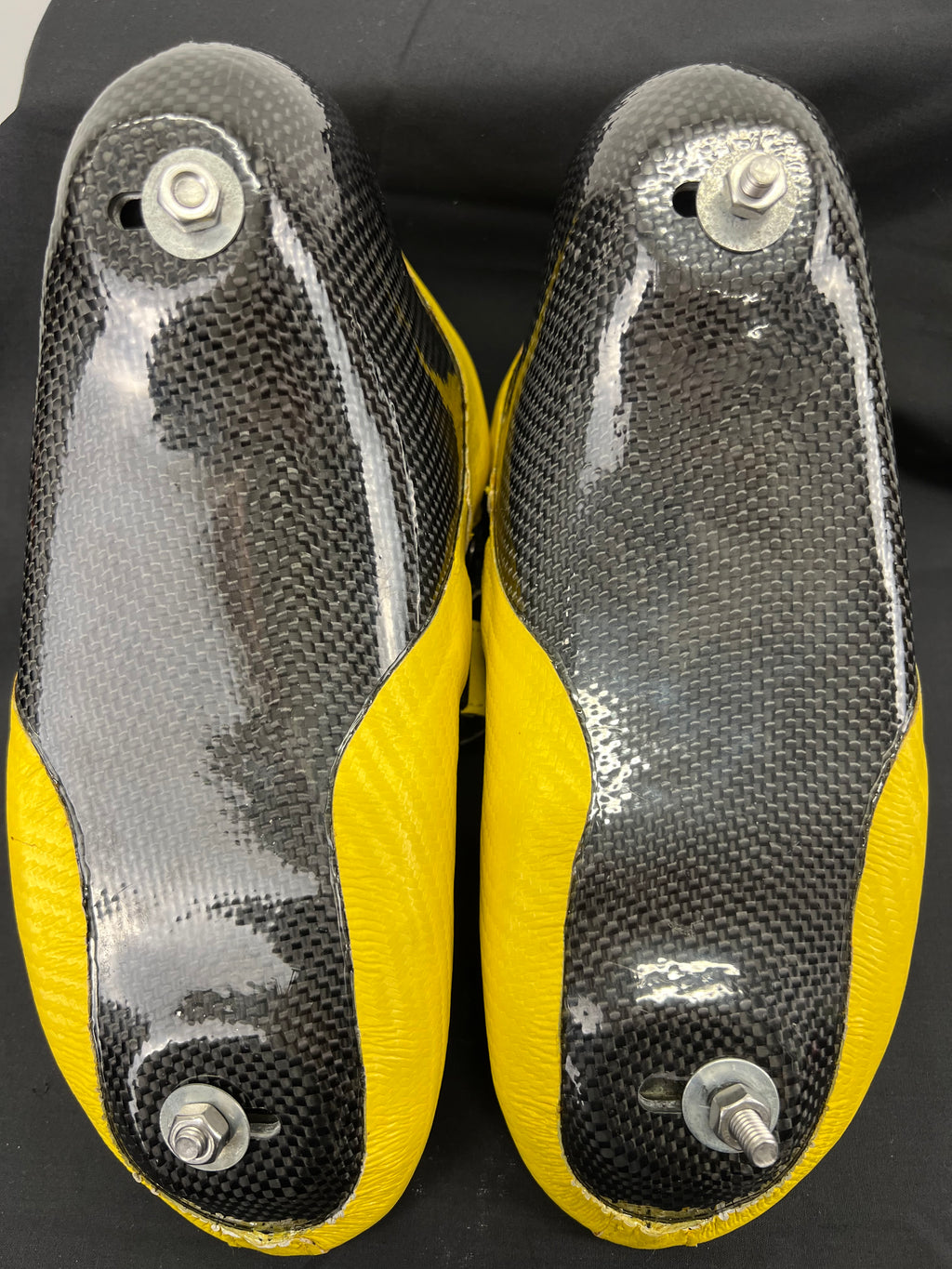 Underneath view of the two skates showing carbon fibre soles with mounting bolts for blades