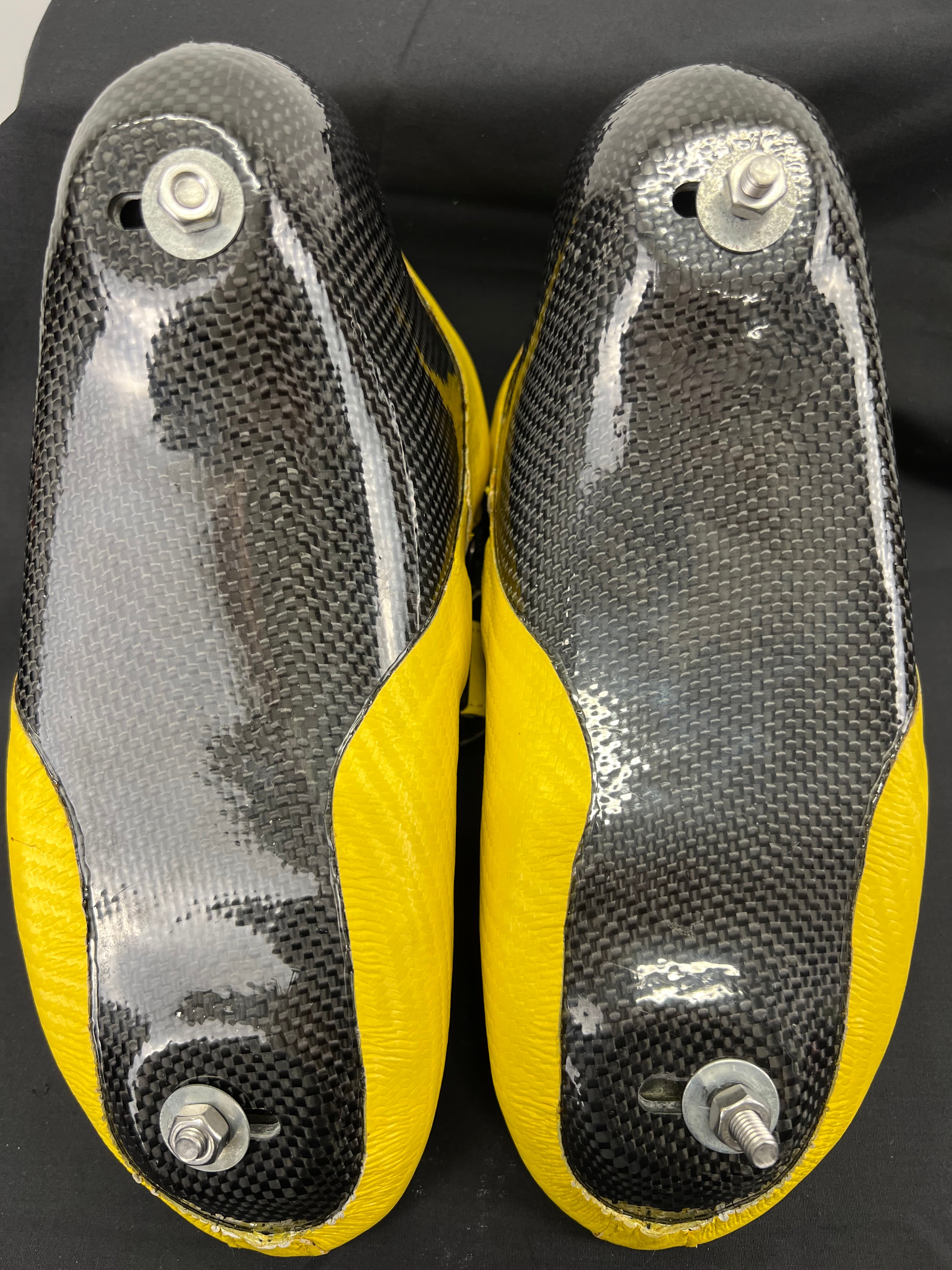 Underneath view of the two skates showing carbon fibre soles with mounting bolts for blades