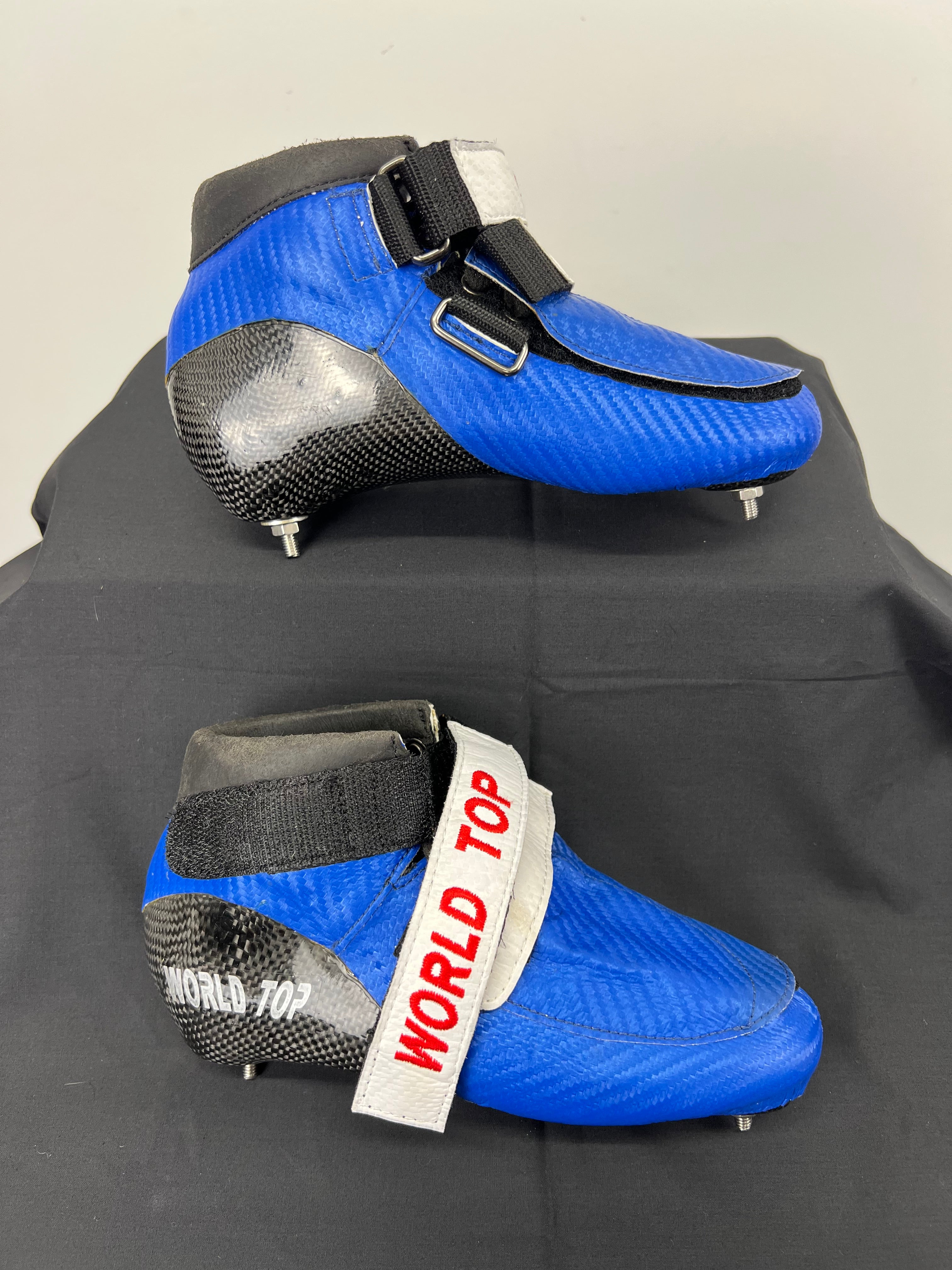Side view of blue World Top short track skate boot with black carbon fibre heel and ankle strap