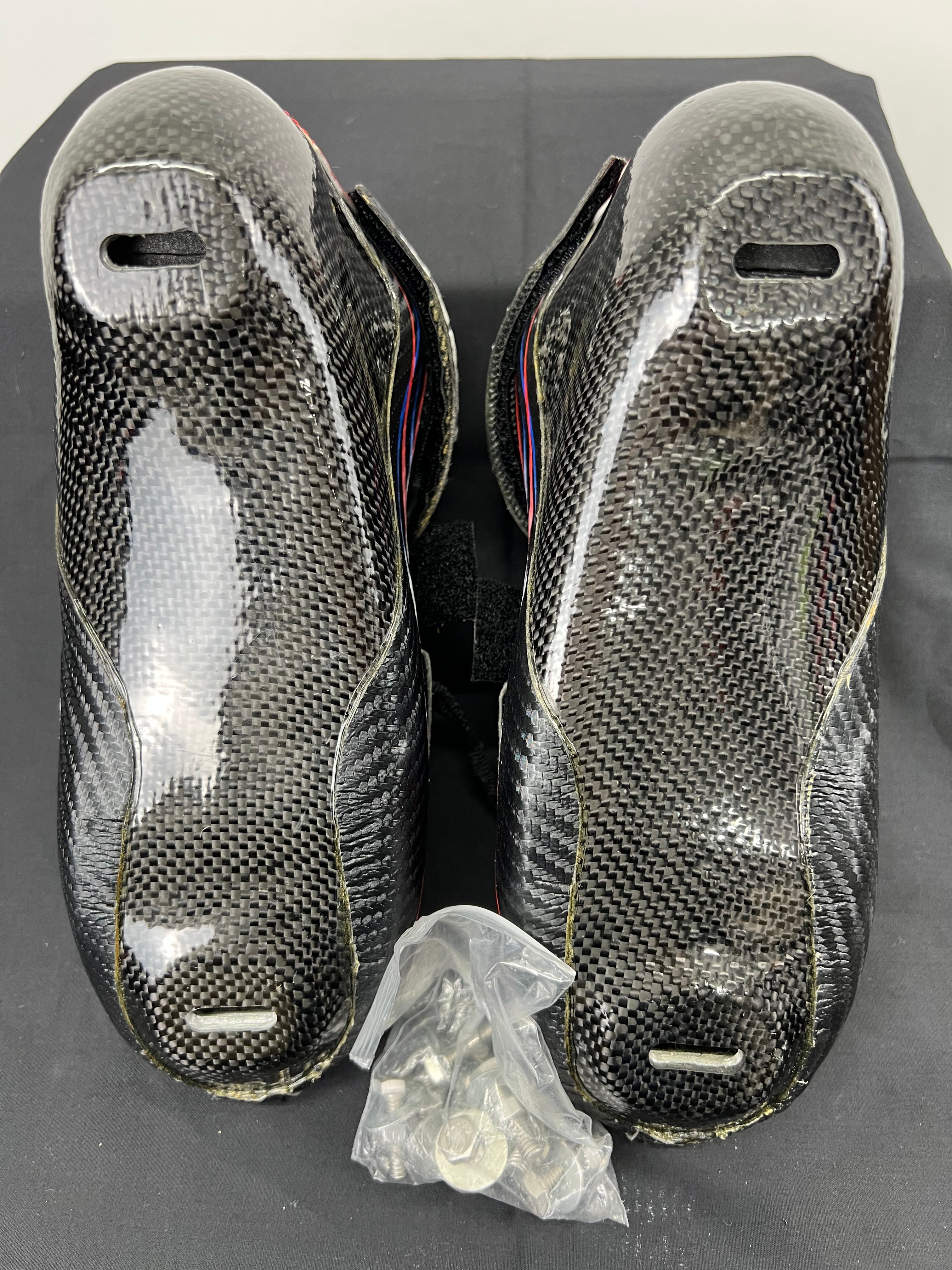 Sole view of carbon fibre short track speed skating boots with mounting holes visible for blade attachment and small packet of screws