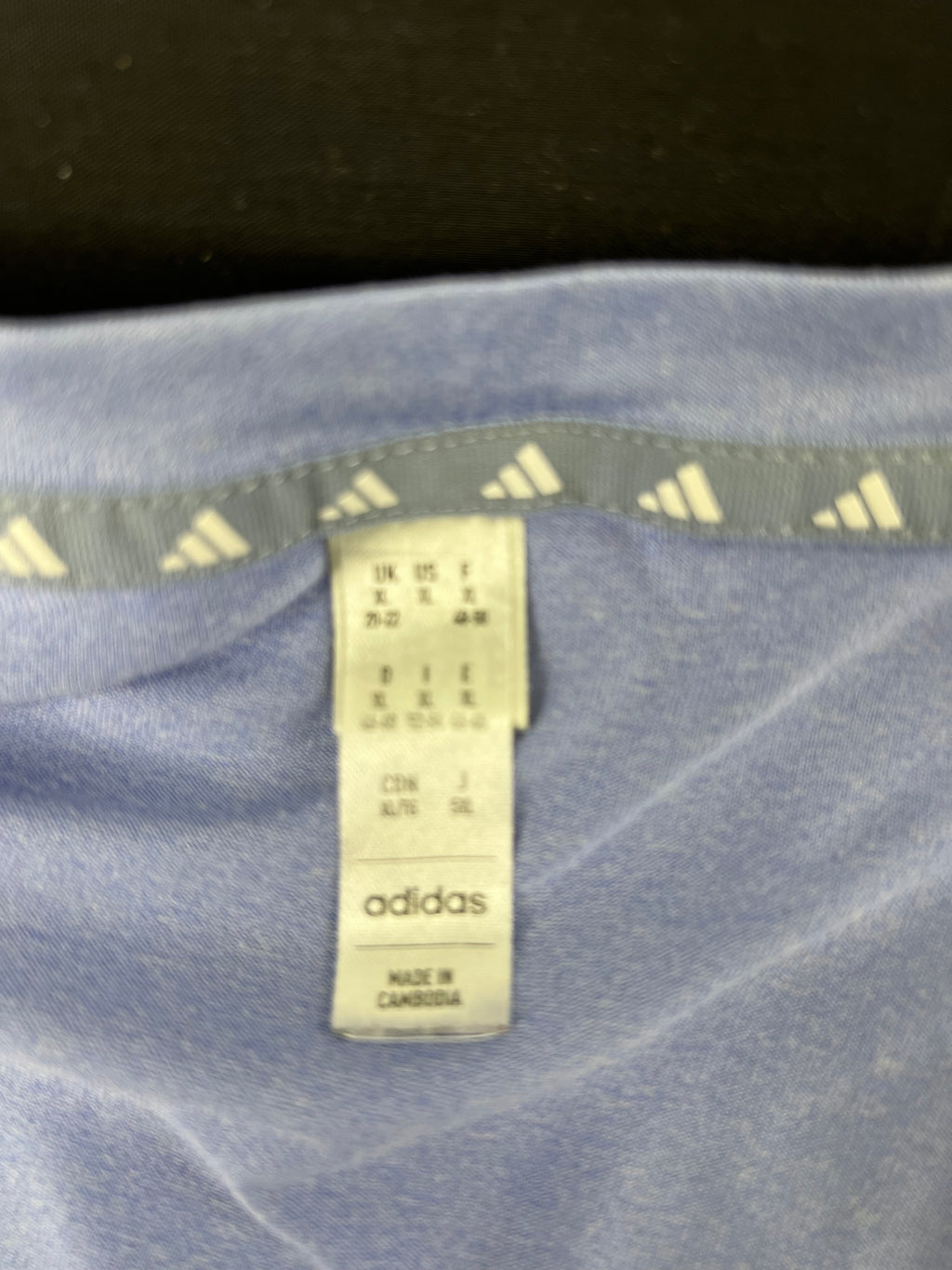 Close-up of Adidas label inside soft blue V-neck t-shirt showing size XL and made in Cambodia
