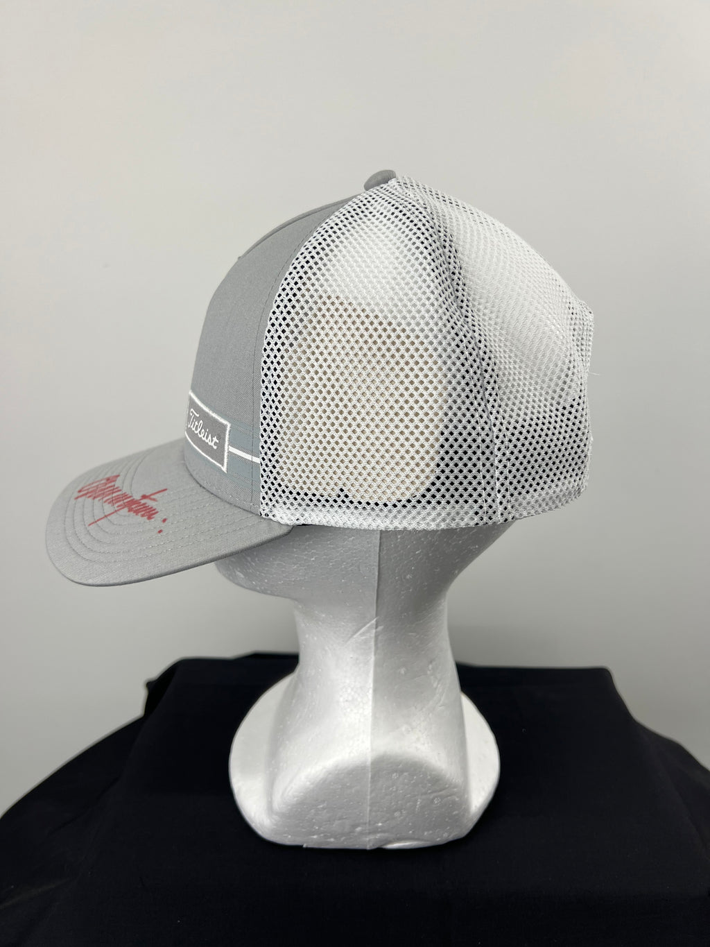 Side angle view of grey front and white mesh back Titleist cap with signature on brim