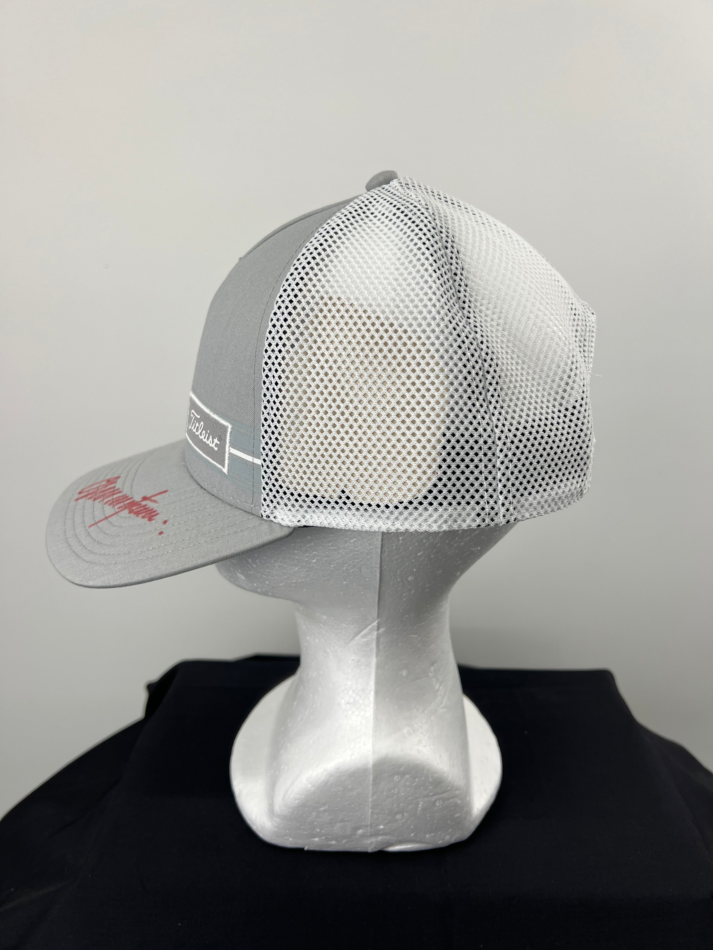 Side angle view of grey front and white mesh back Titleist cap with signature on brim