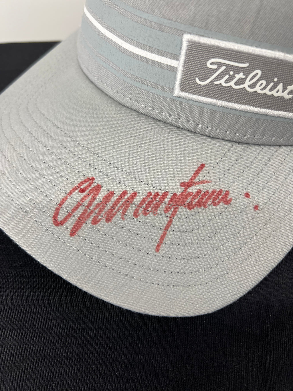 Close-up of Colin Montgomerie signature in red ink on the curved brim of the grey Titleist cap