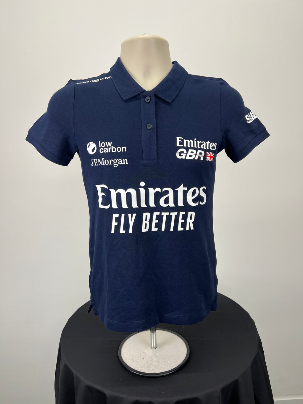 Front view of women's navy blue Emirates GBR x Henri Lloyd polo shirt with multiple logos