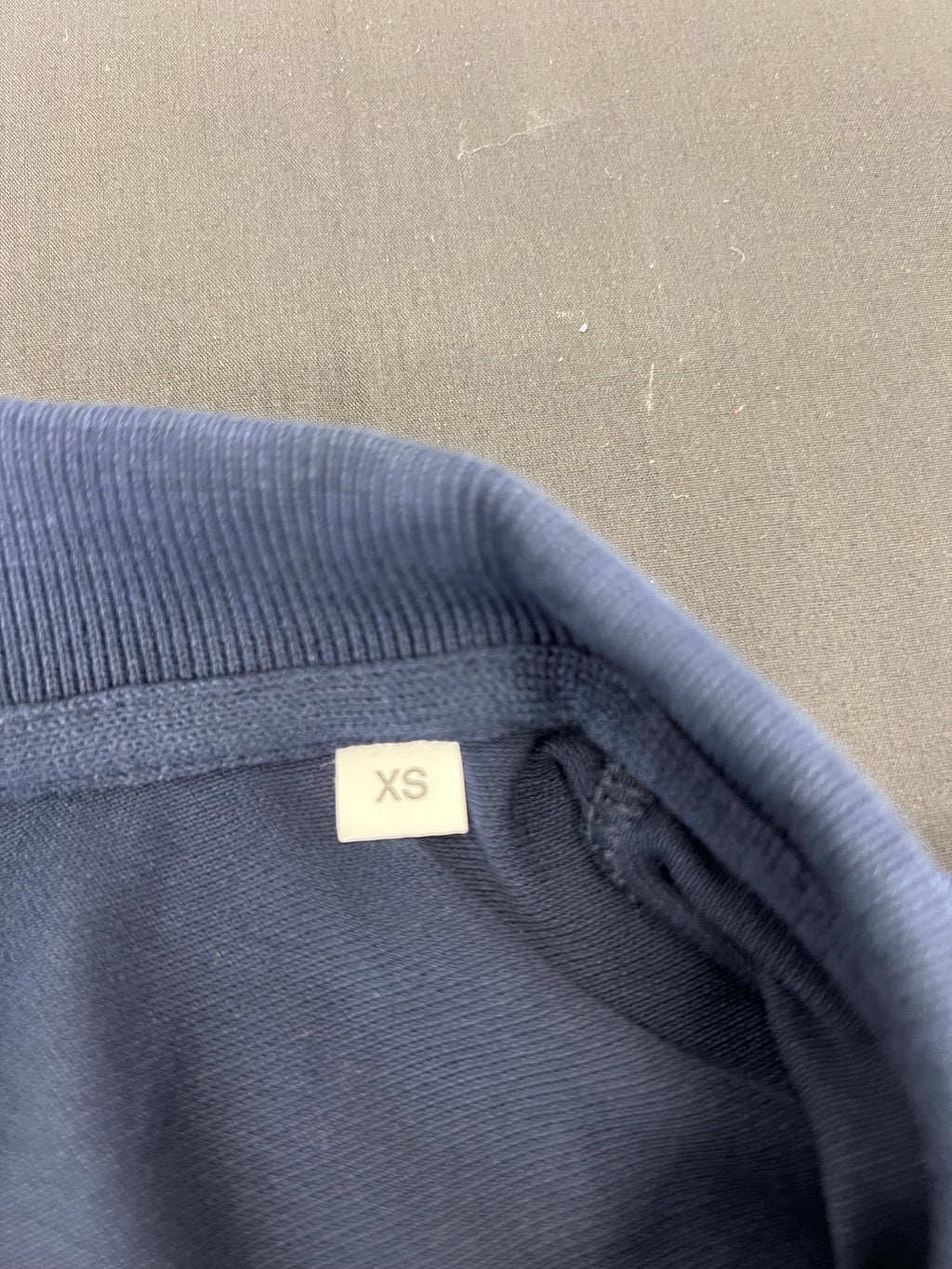 Close up of XS size label inside collar of navy blue polo shirt