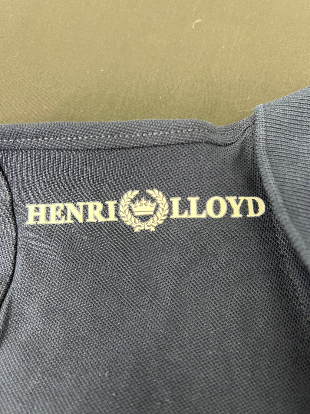 Close up of Henri Lloyd logo printed inside shoulder area on navy polo shirt