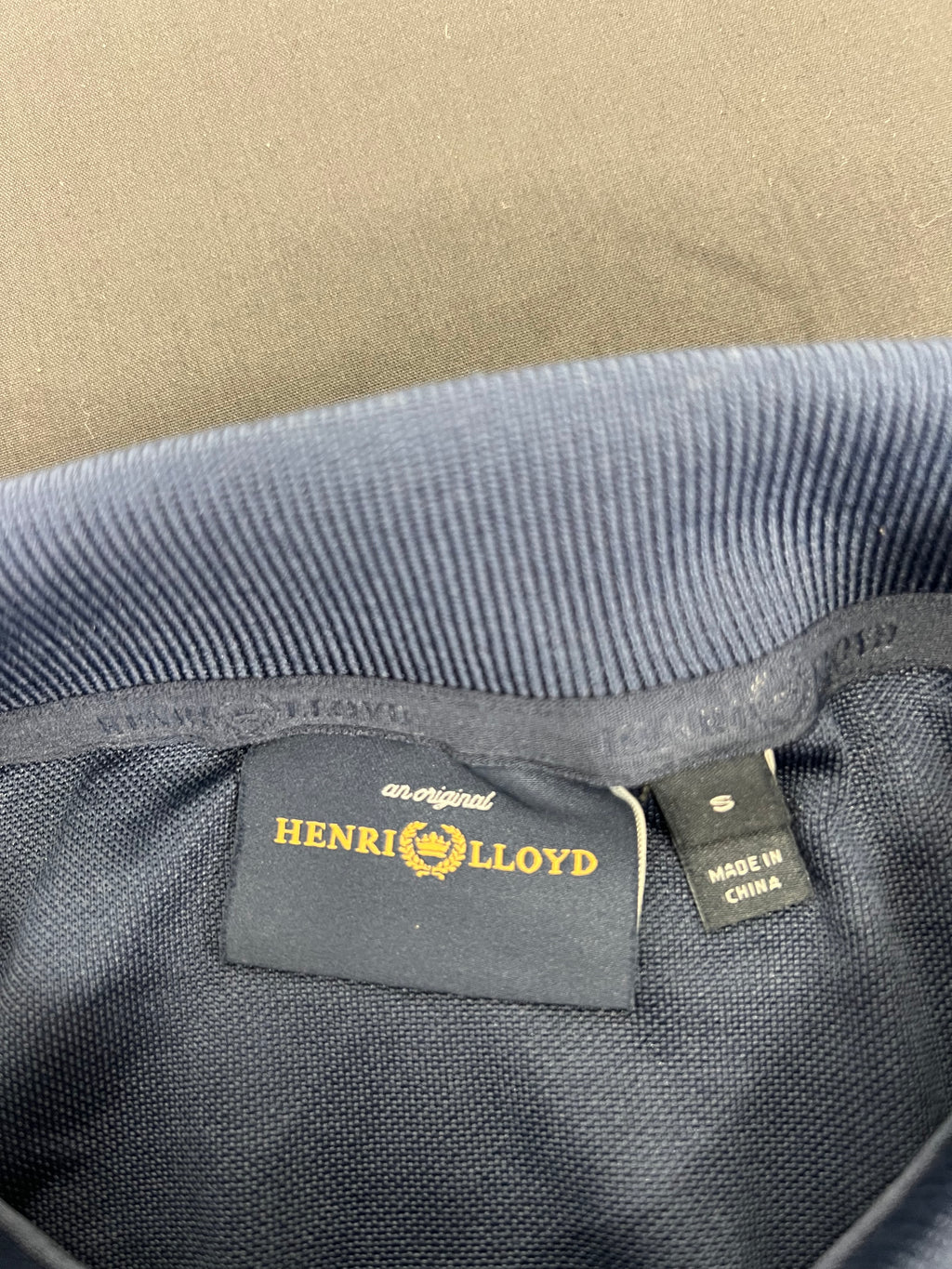 Close-up of Henri Lloyd brand label and 'made in China' fabric tag inside collar of navy polo