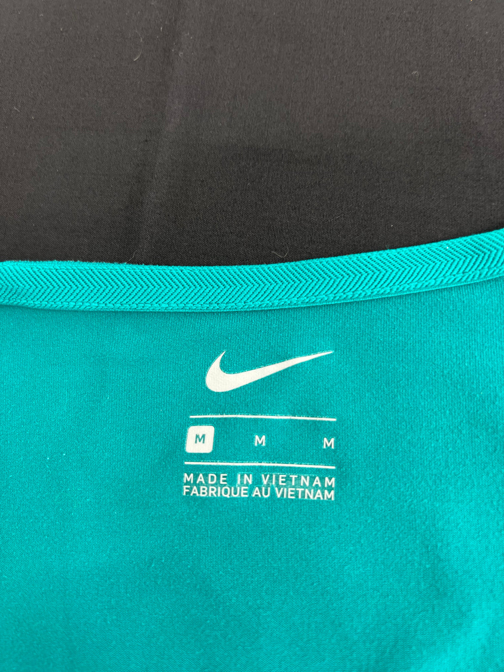 Close-up of inside label showing Nike logo and size medium on teal fabric