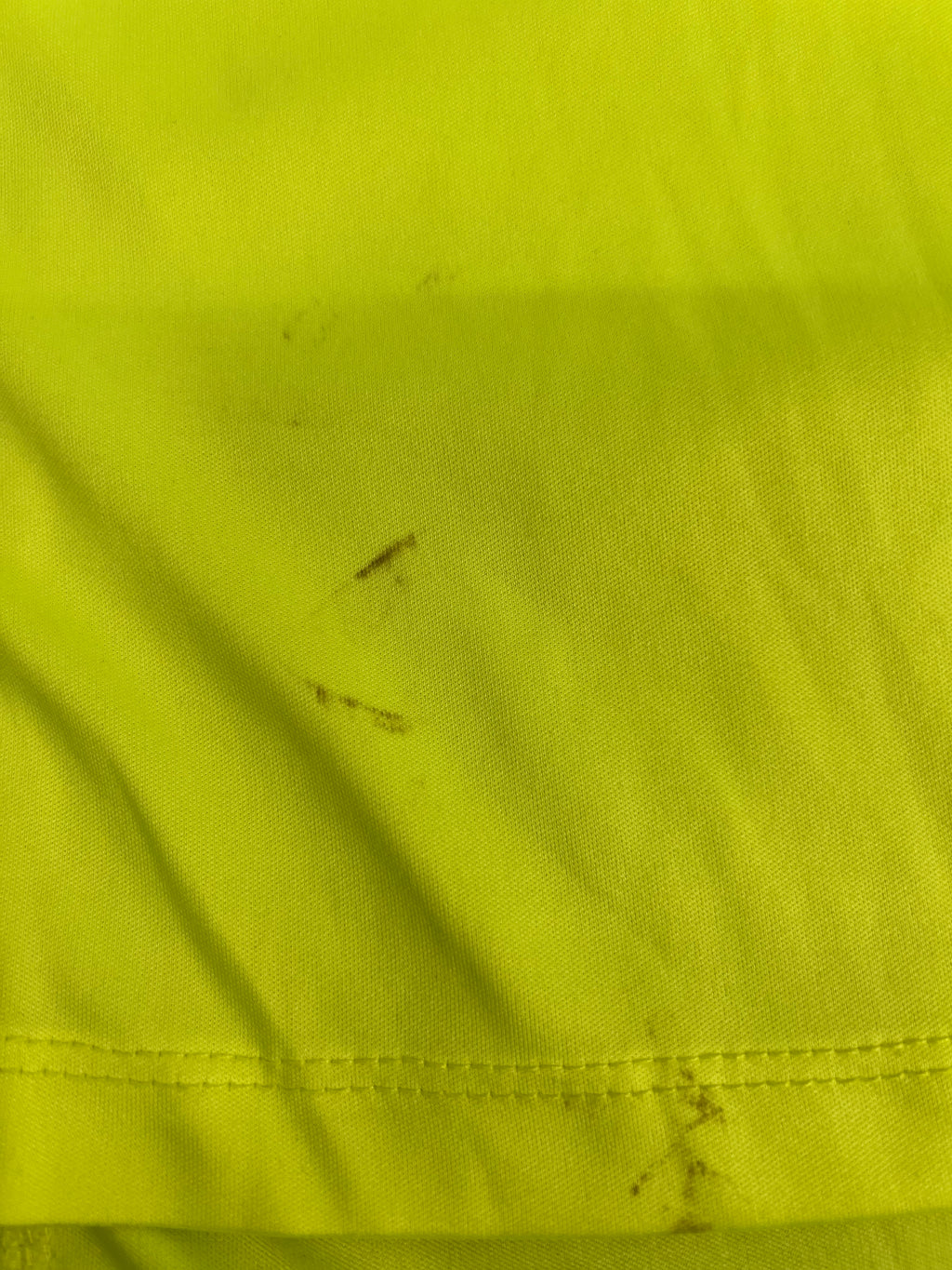Close-up of minor dirt marks on bright green running top near hem